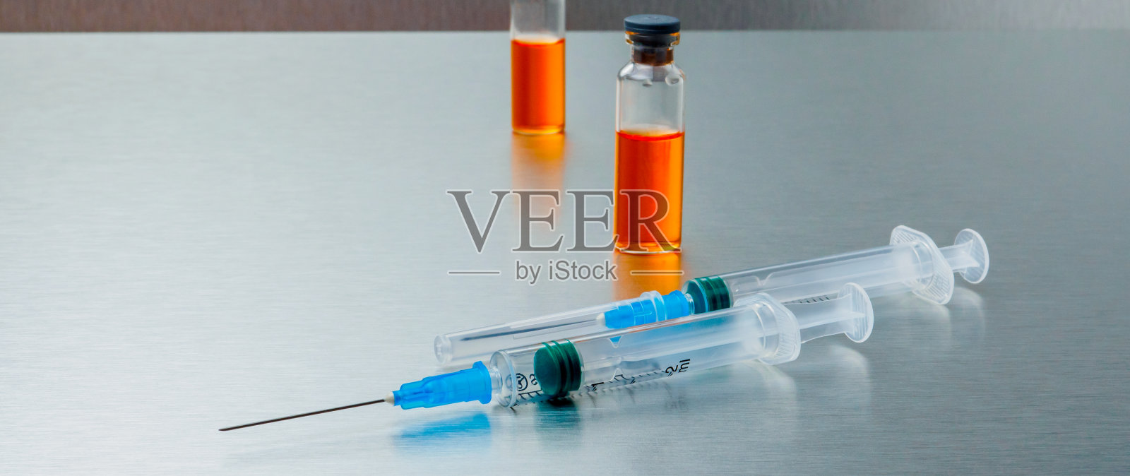 横幅。特写注射注射器和安瓿与橙色冠状病毒疫苗在银色铝背景。Covid-19大流行医学概念。照片摄影图片