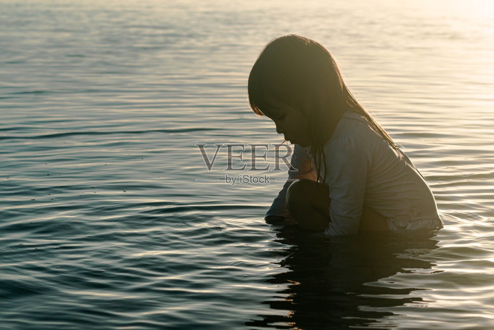 一个沮丧的小女孩坐在海滩外面，悲伤的孩子照片摄影图片