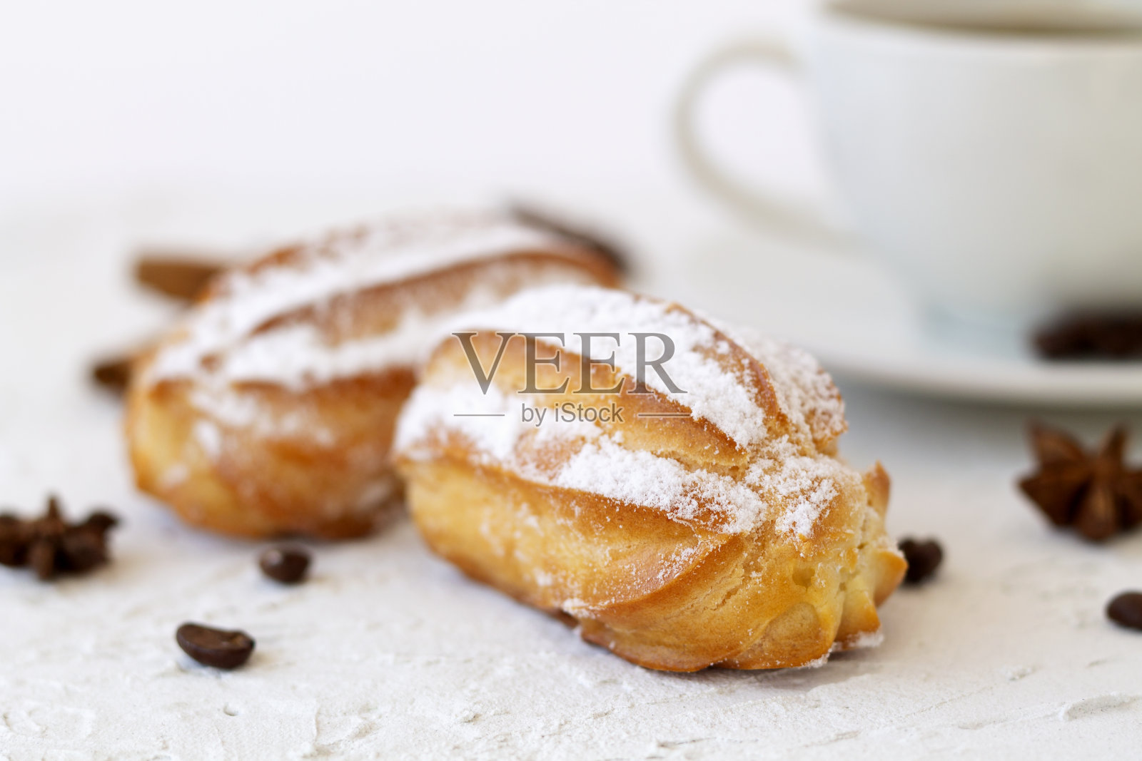 近景香草泡芙在一个盘子上的背景。咖啡杯，咖啡豆，八角，肉桂棒放在白色的桌子上。副本的空间。传统的法国美味甜点。照片摄影图片