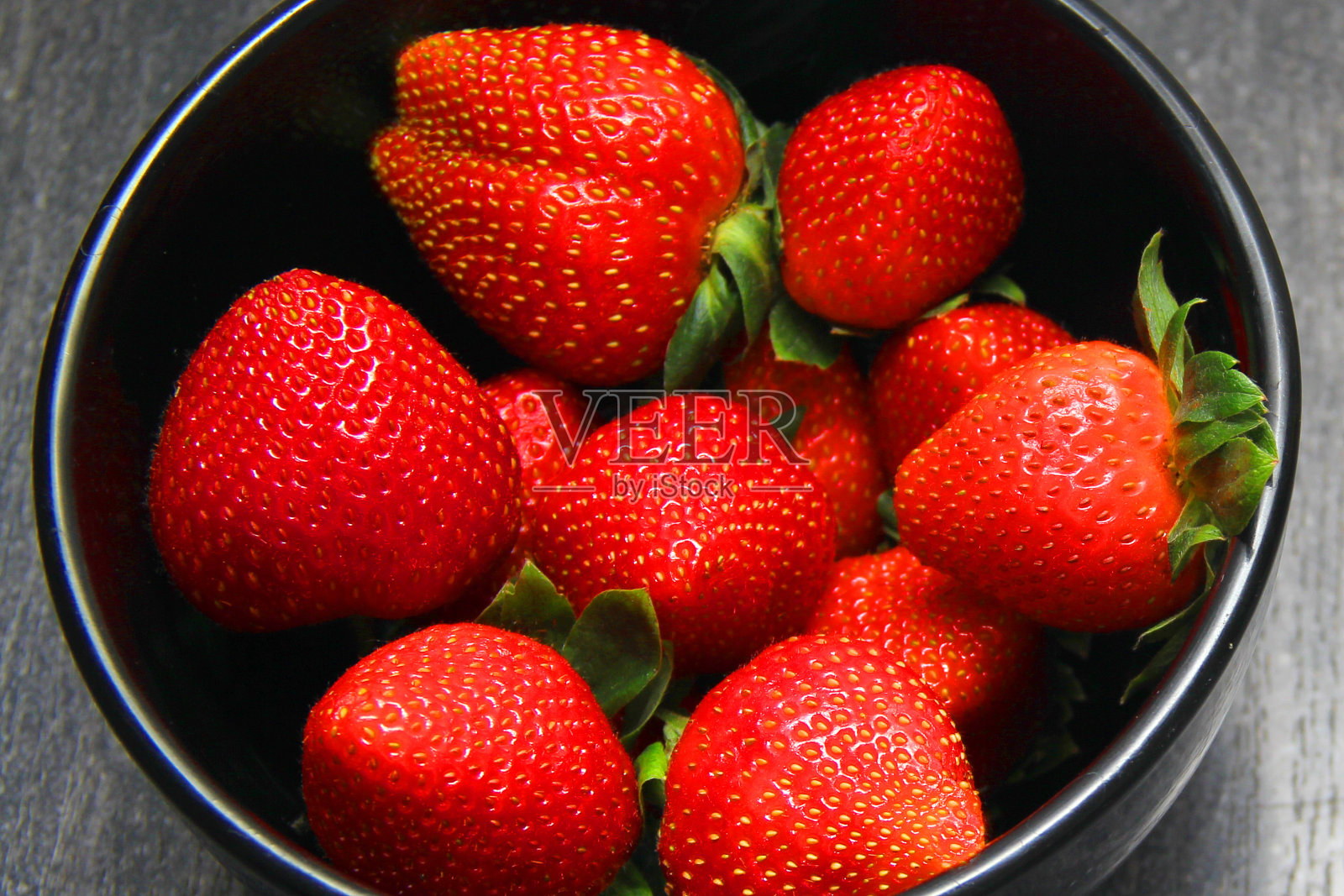 红色的草莓水果放在黑色的盘子里。复古灰木背景照片摄影图片