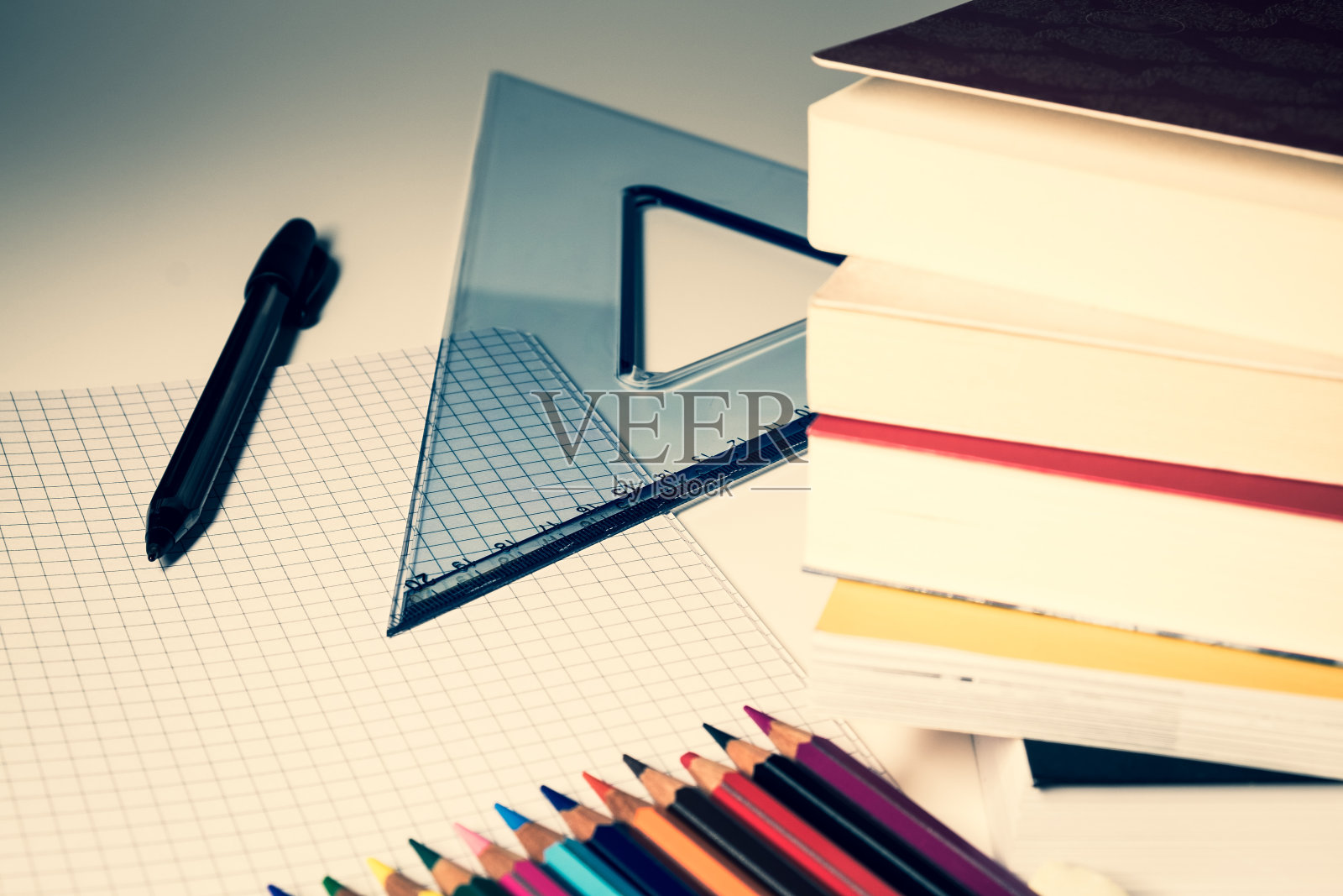 前台是一堆书，背景是一个专门的绘图支架，一支钢笔和彩色蜡笔被放在一张方形纸上。照片摄影图片