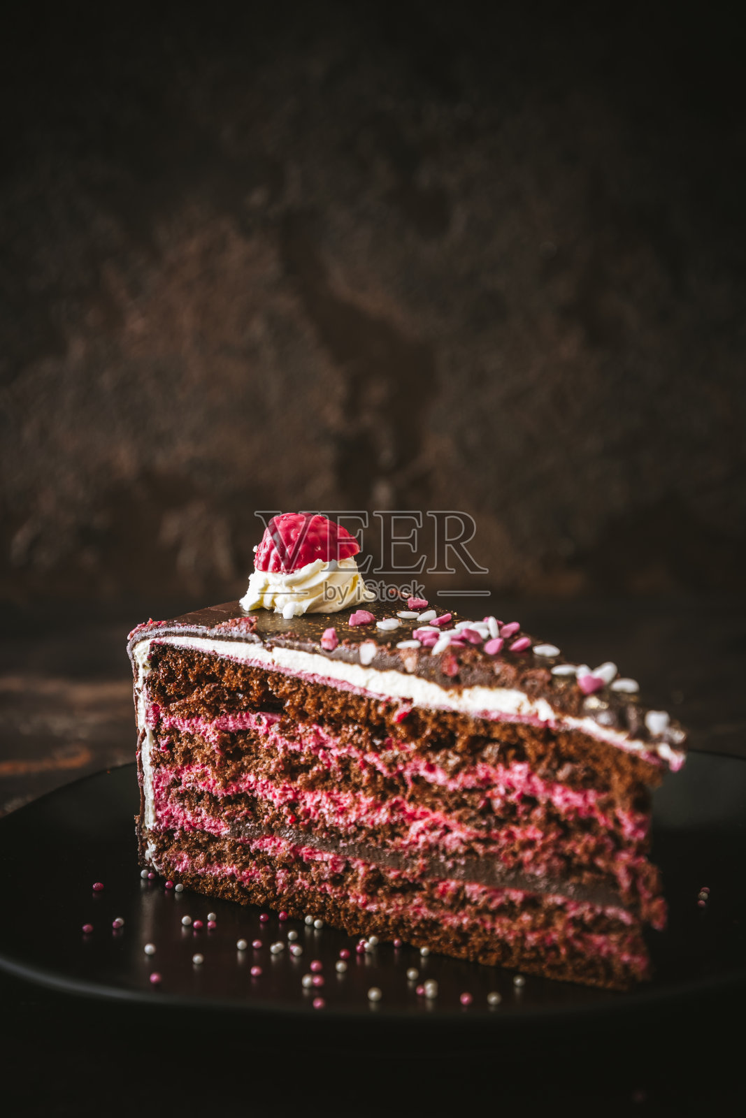 一块覆盆子巧克力蛋糕放在一个黑色盘子上，背景为深棕色，与复制空间垂直照片摄影图片