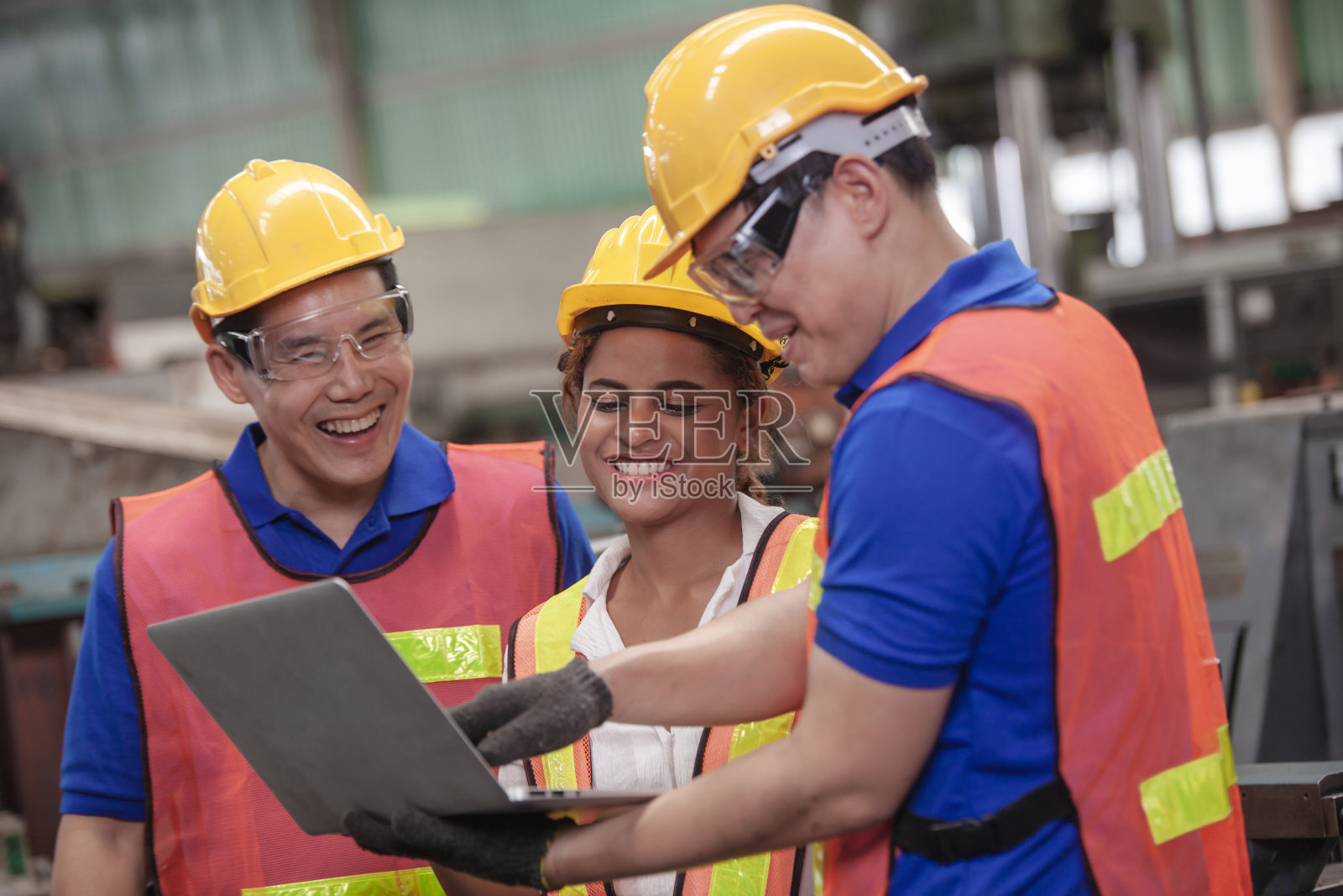 男性和女性工业工程师在使用笔记本电脑时与工厂工人交谈。在工厂里拿着笔记本电脑的工业工程师，照片摄影图片