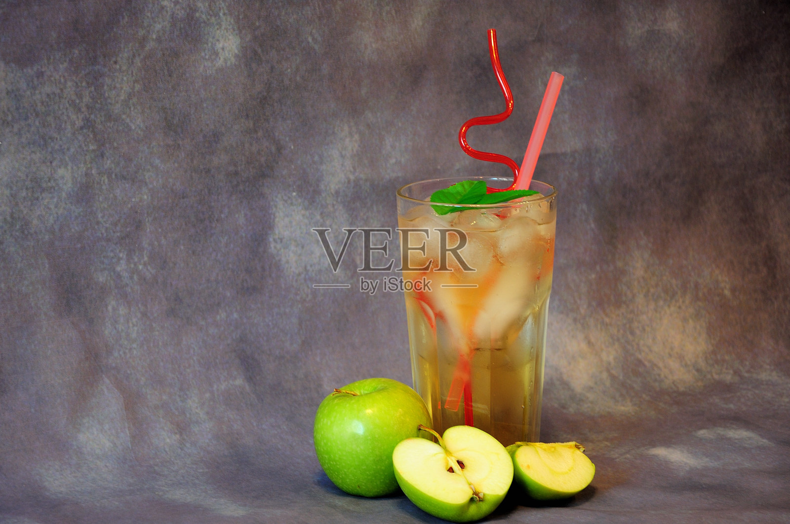灰色的背景上放着成熟的青苹果和一杯带冰的果汁。照片摄影图片