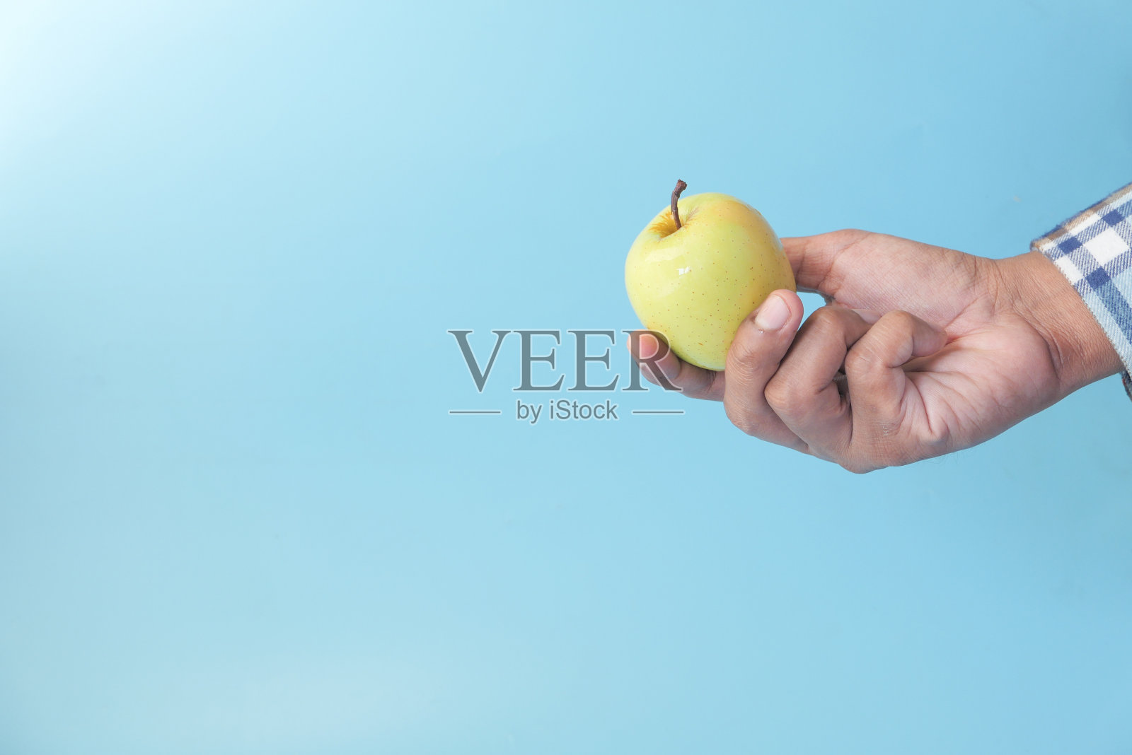 在蓝色的背景下，手拿着绿苹果照片摄影图片
