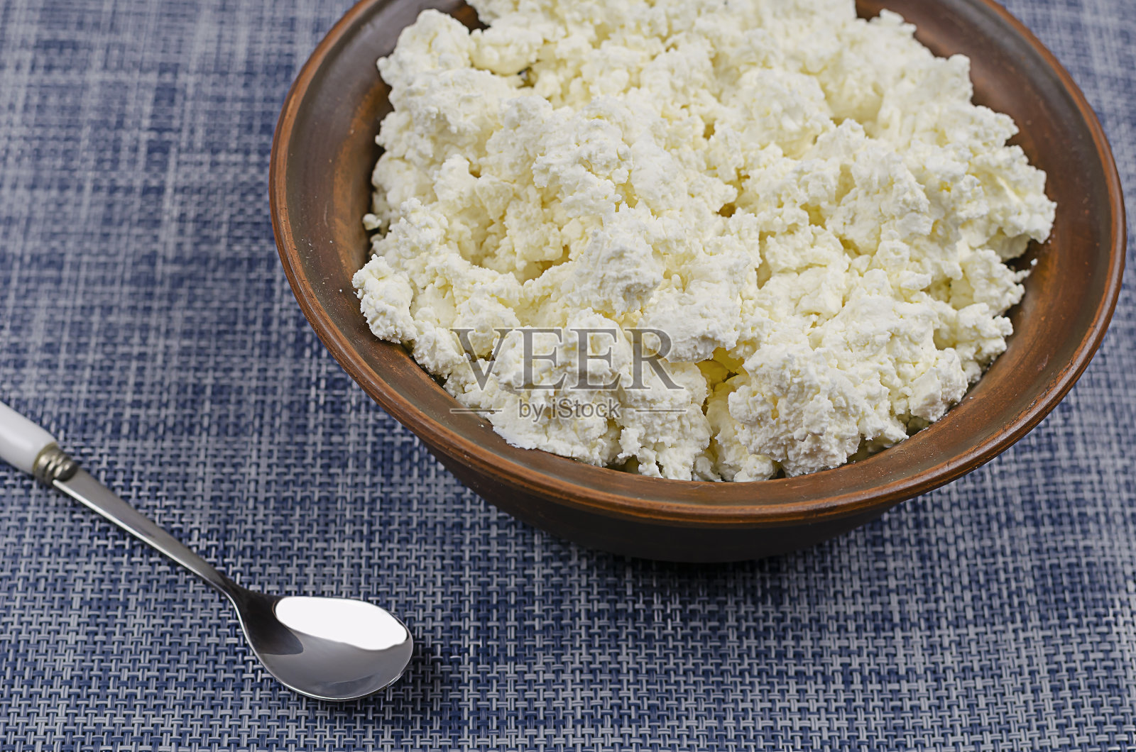 一大碗凝乳和一个勺子，在蓝白色的背景上。照片摄影图片