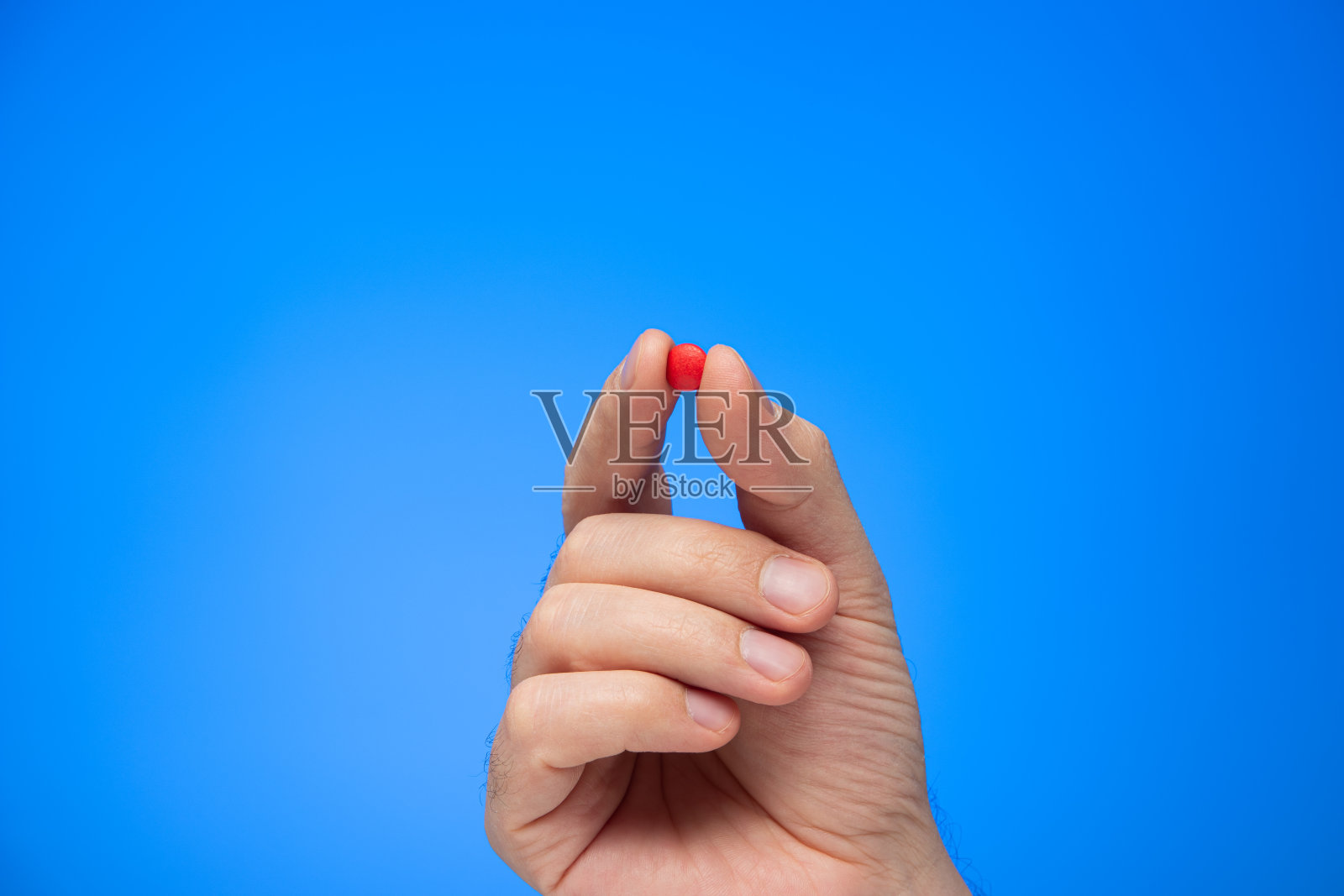 红色的丸子夹在手指间，白种人的手孤立在蓝色的背景下拍摄照片摄影图片