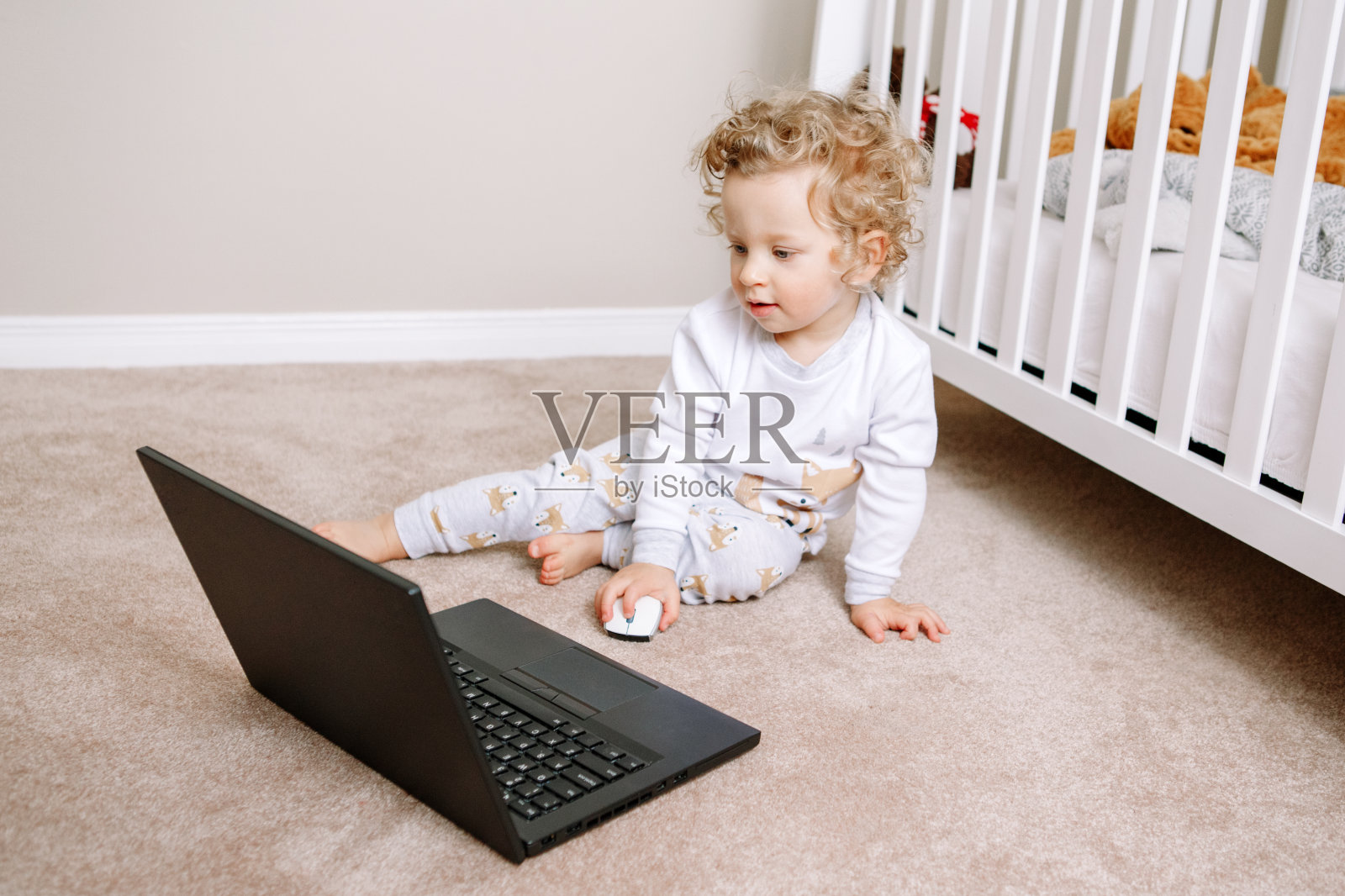 可爱的金发卷曲的蹒跚学步的小男孩在笔记本电脑上工作。小孩子在使用科技。早期教育和发展。视频聊天，视频通话。孩子们看电脑的时间。照片摄影图片