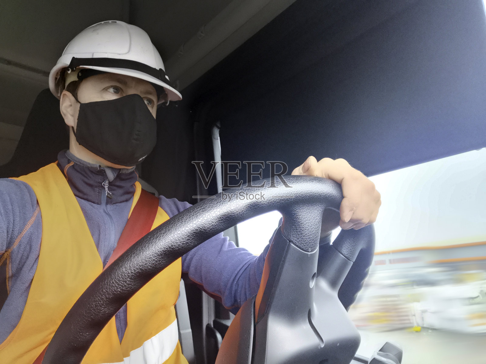 卡车司机从后面的方向盘戴面罩头盔和高Vis背心照片摄影图片