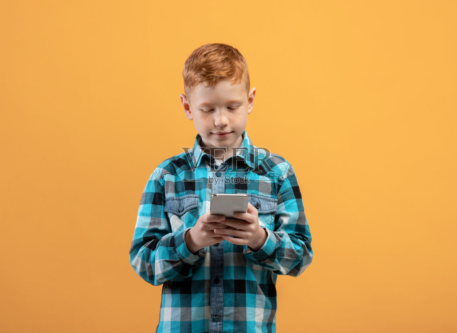 可爱的姜黄色小孩，手机是黄色的照片摄影图片