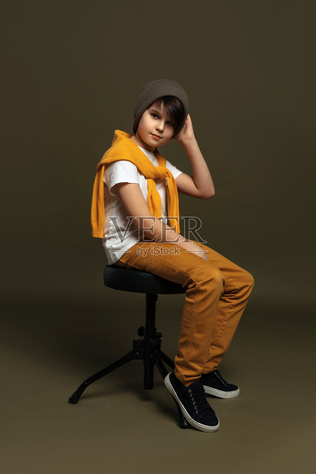 帅气时尚的年轻男孩坐在工作室的椅子上，在绿色的背景。休闲风格。时尚的工作室拍摄照片摄影图片