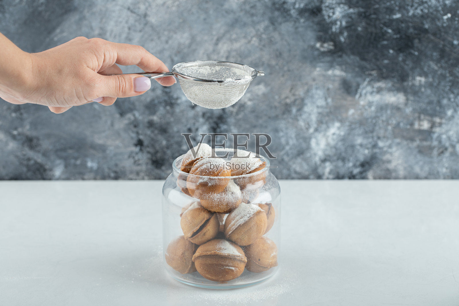 女性的手在胡桃形状的饼干上撒糖粉照片摄影图片