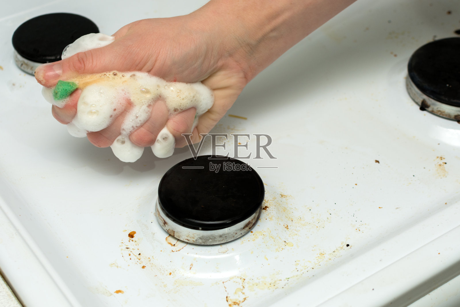 在一个女人的手里，一块海绵泡沫，清洁一个肮脏的炉子。这个想法就是做家务，保持清洁。横向照片，大计划。照片摄影图片