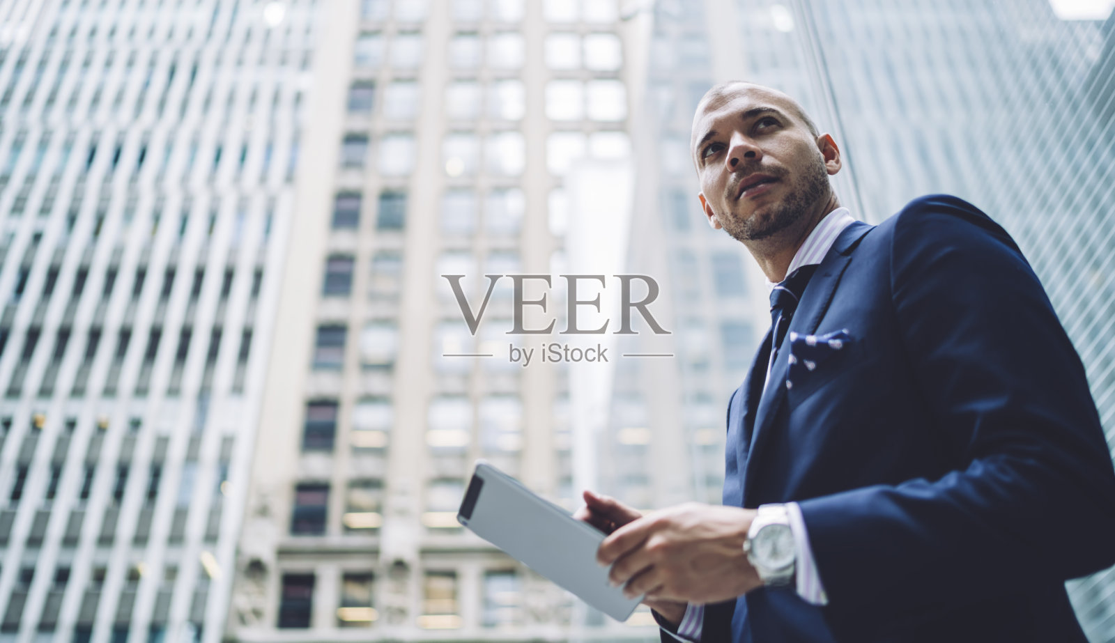 下图是一位30多岁的白种教育工作者在平板电脑上浏览教育网站时的目光，这位智能教师穿着正式优雅的套装，使用现代科技在市中心照片摄影图片