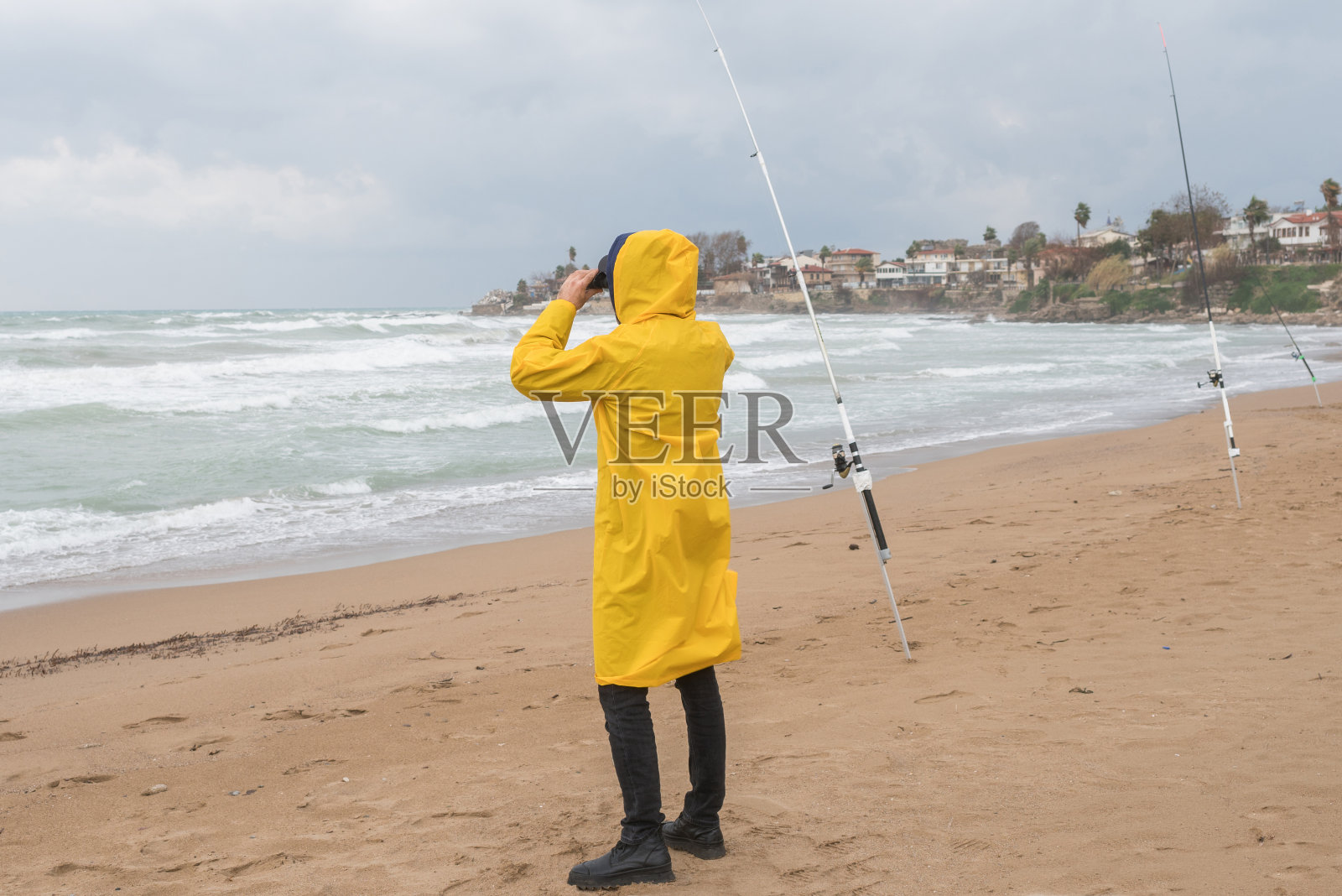 在恶劣的天气里，渔民在海滩上用双筒望远镜望向别处照片摄影图片