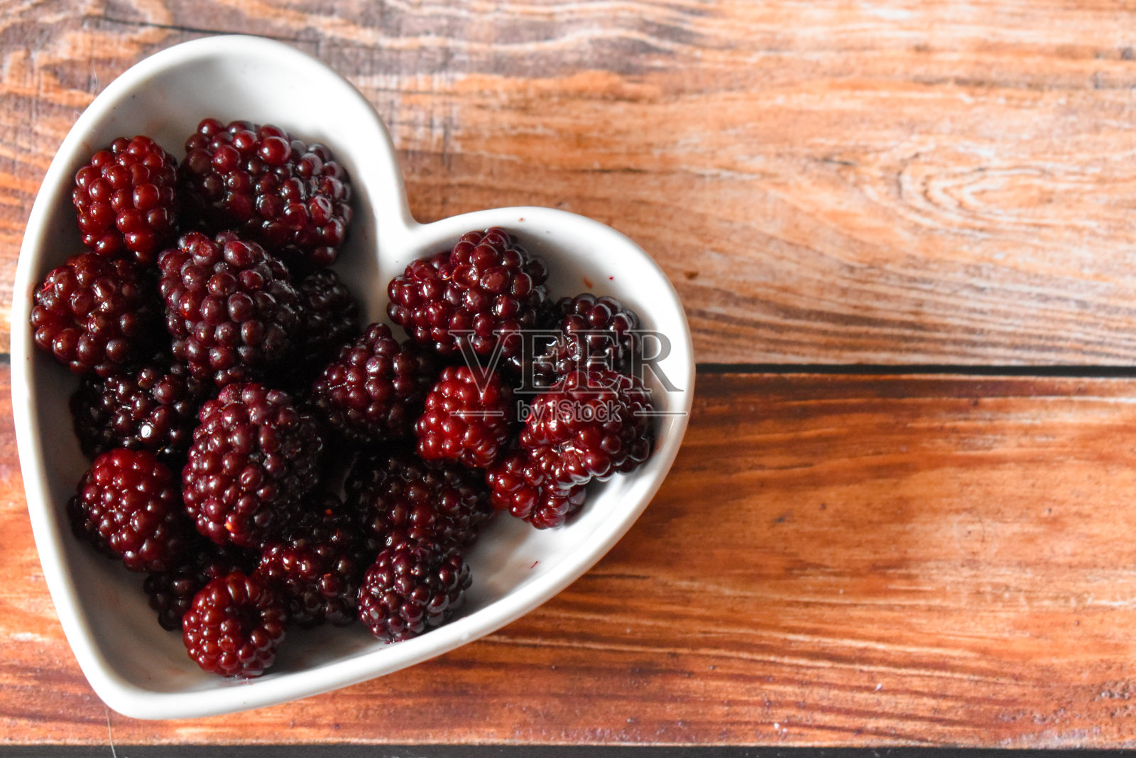 黑莓放在一个心形的碗里，放在一张木桌上照片摄影图片