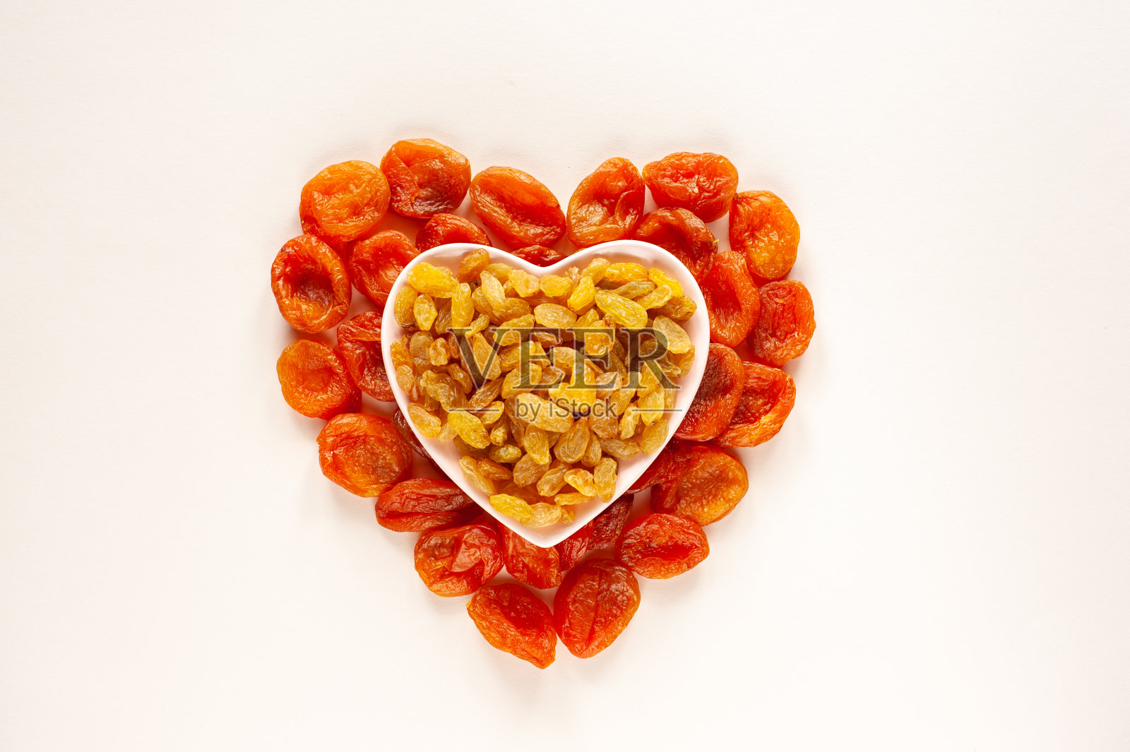 杏干和葡萄干以两颗心的形式摆放在米黄色的背景上。健康饮食。对心脏健康有益的食物。为孕妇准备的糖果。素食食物。从以上观点。情人节。照片摄影图片