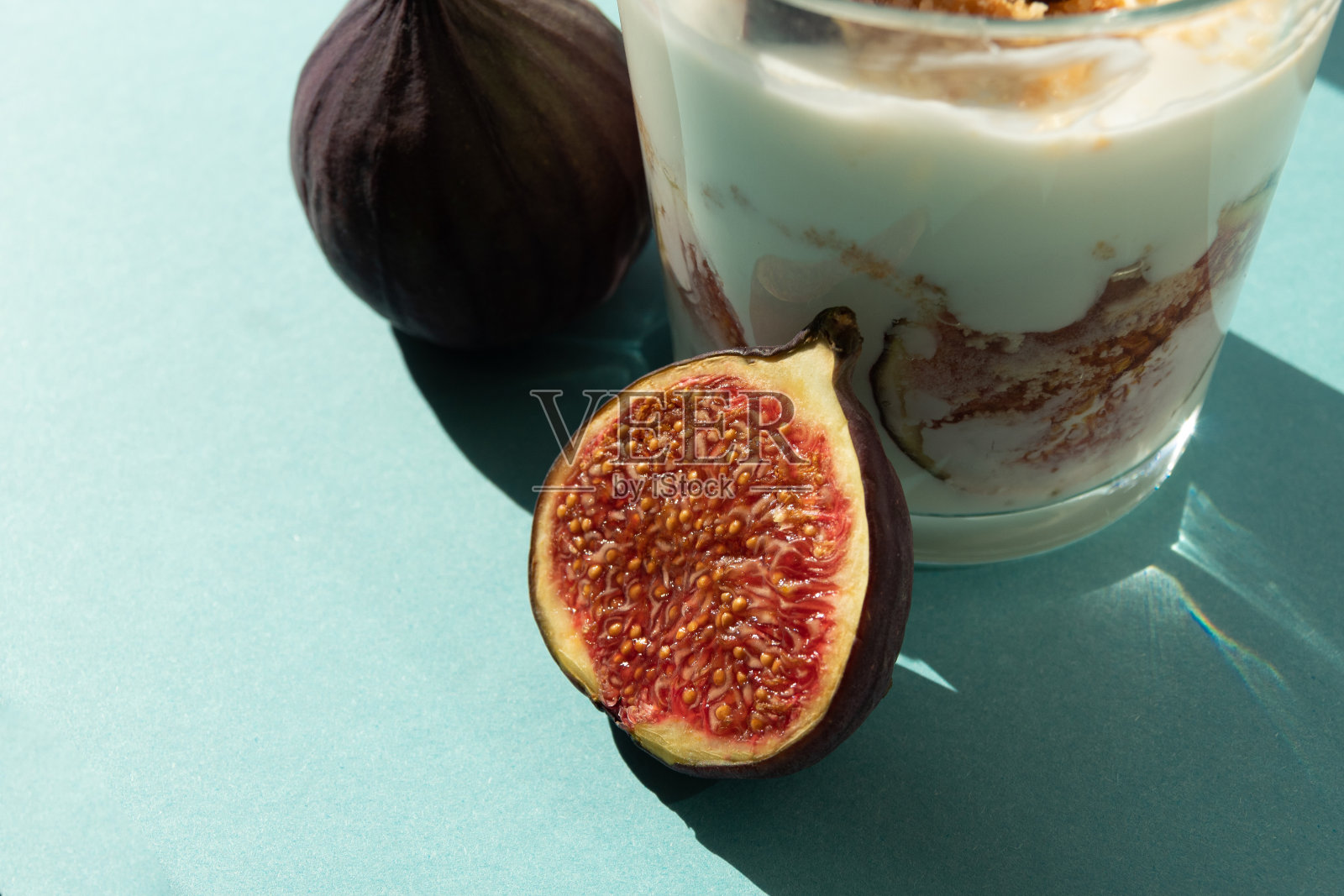 阳光下，半颗成熟的无花果和一杯甜点放在一起。夏天的收获。有选择性的重点。照片摄影图片