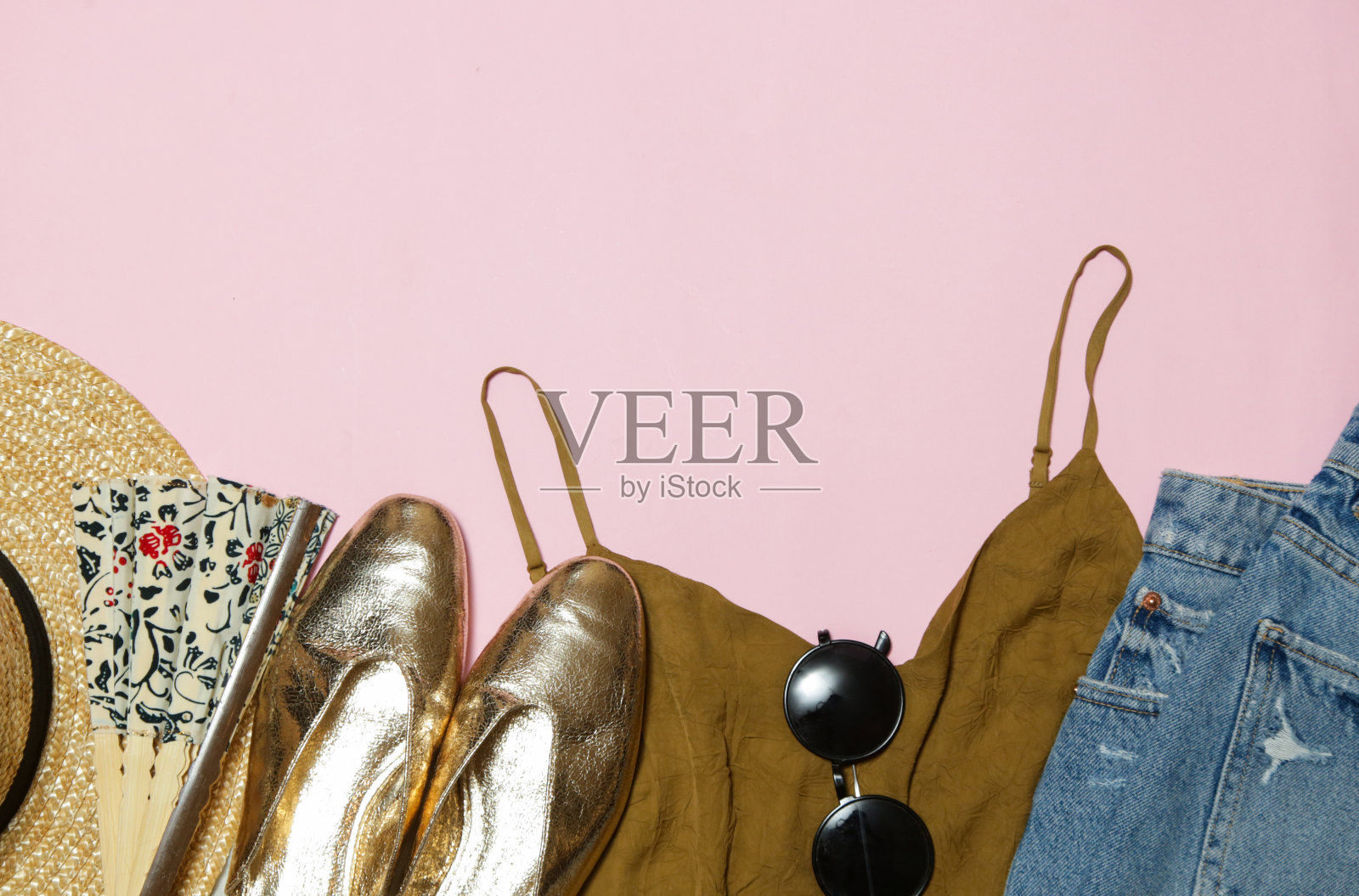 粉色背景的夏装，蓝色牛仔裤，草帽和金色配饰。女性夏季时尚单品。照片摄影图片