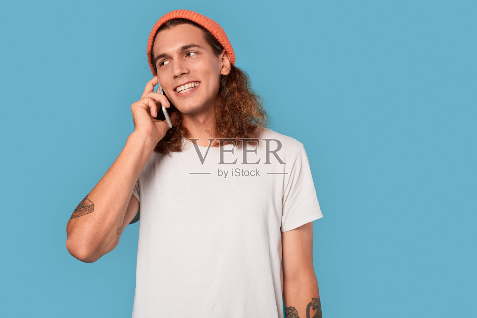 自由泳。卷发的家伙戴着帽子孤立地站在蓝色上用智能手机聊天，笑得很开心照片摄影图片