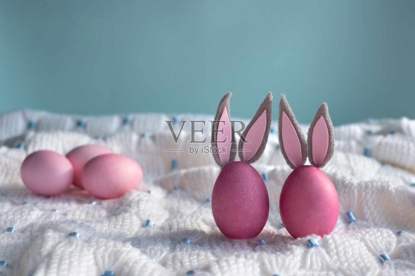 粉红色的复活节彩蛋与兔子耳朵特写在白色针织格子在一个蓝色的背景。照片摄影图片