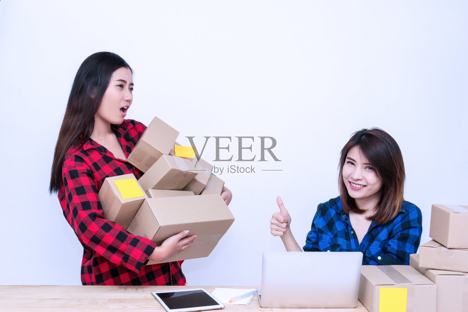 两个年轻的女人开始他们的中小企业业务。商业女性团队私人工作在家庭办公室使用笔记本电脑在白色的背景。包装配送网络购物服务广告客户。照片摄影图片