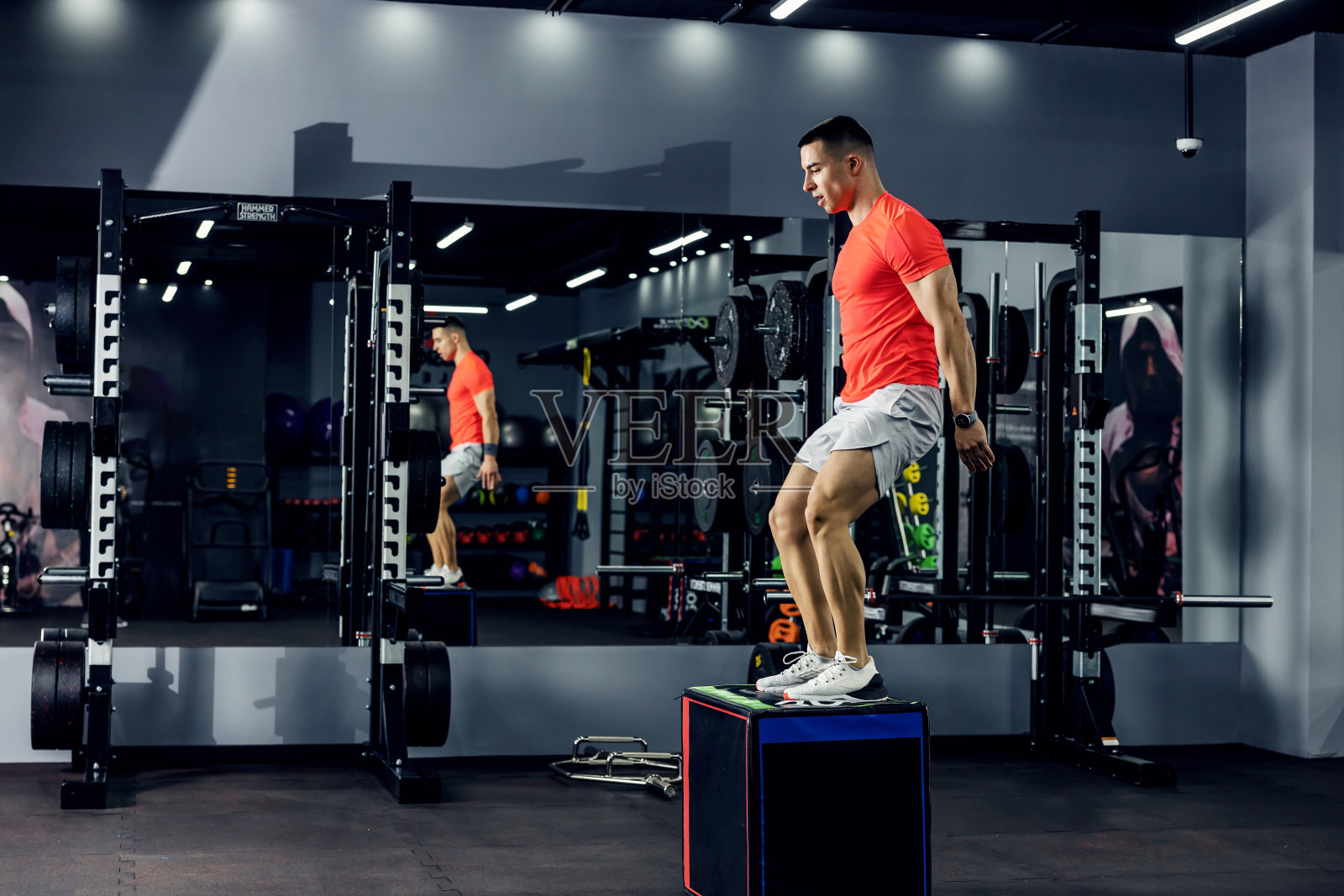 一个强壮的年轻人在他的腿和手臂肌肉表达刚刚降落在一个踏板在健身房。运动服，个人训练照片摄影图片