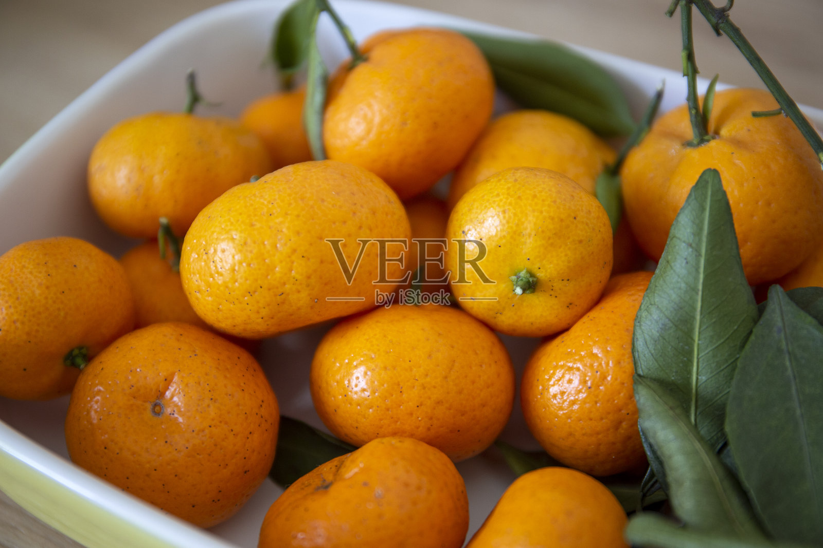 鲜桔子和叶子放在白色陶瓷盘子上的特写镜头照片摄影图片