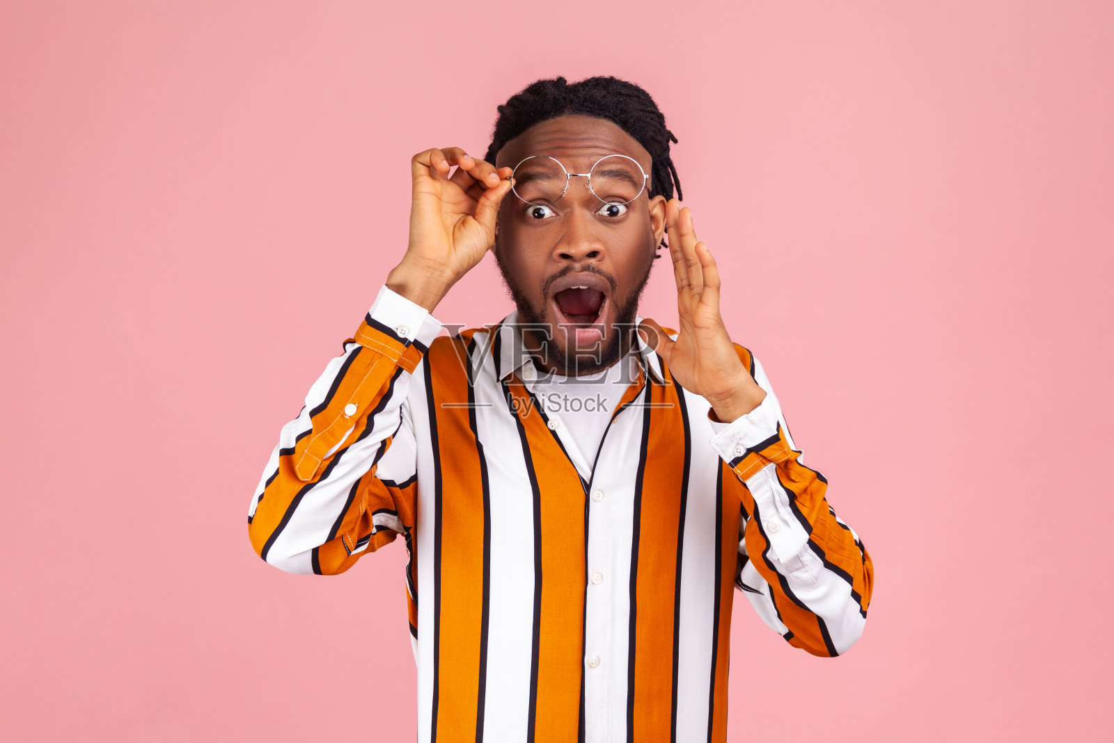 我真不敢相信。震惊不知所措的非裔美国人与发辫在明亮的条纹衬衫看着相机与大眼睛，惊讶照片摄影图片