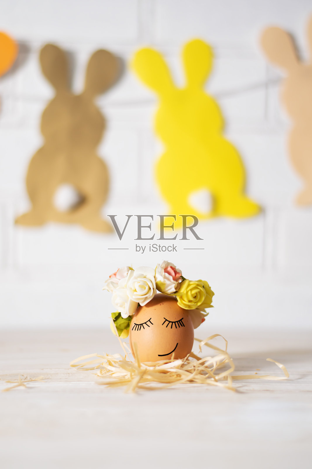 复活节彩蛋和滑稽的脸。有趣的复活节彩蛋装饰黄玫瑰花环和纸兔子。复活节彩蛋正在睡觉。照片摄影图片