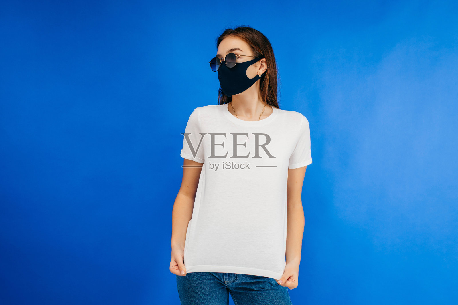 时尚的女孩戴着眼镜和面具，穿着白色t恤在工作室里摆姿势在蓝色的背景照片摄影图片