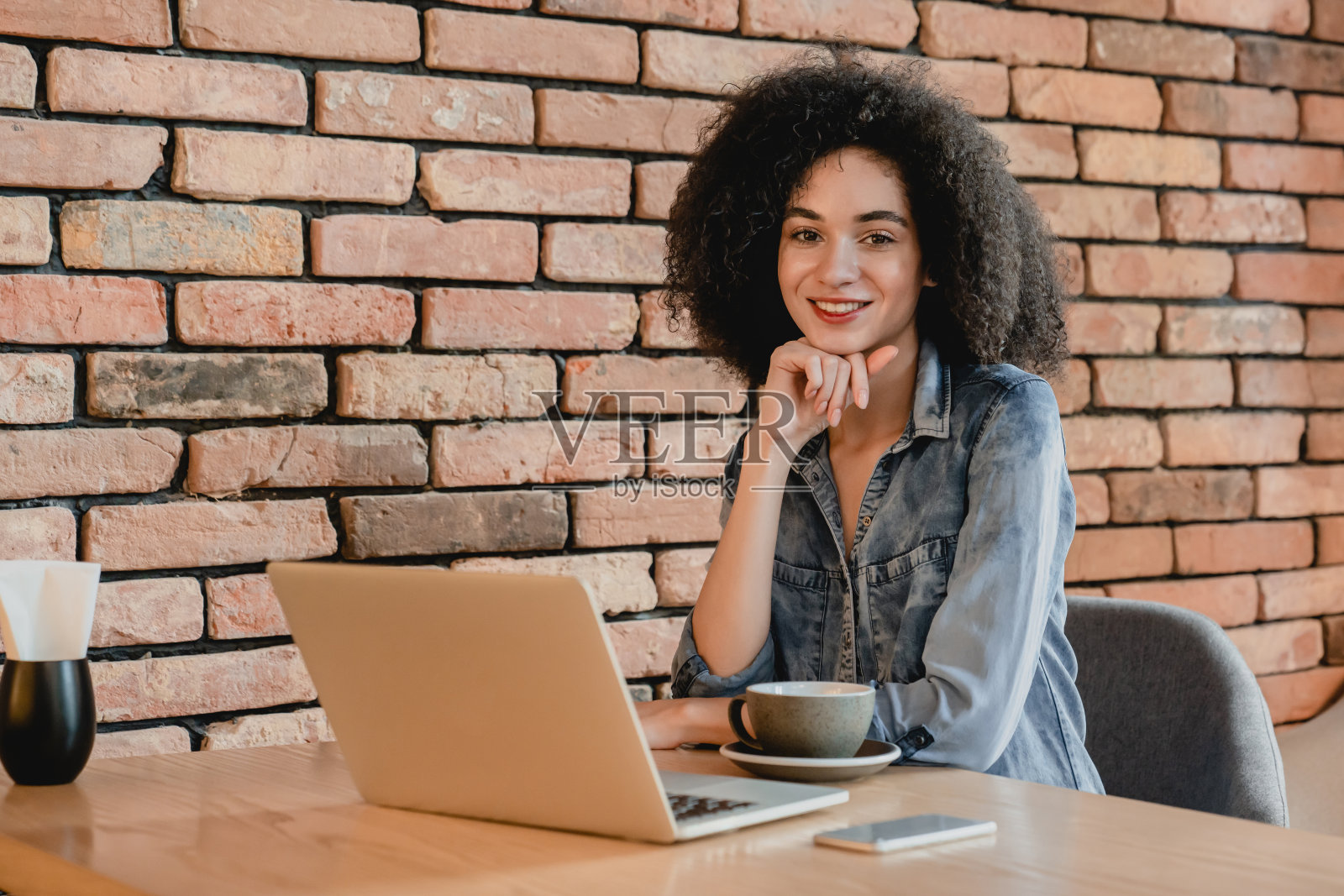 在小咖啡馆里使用笔记本电脑的年轻漂亮的非洲女孩肖像照片摄影图片