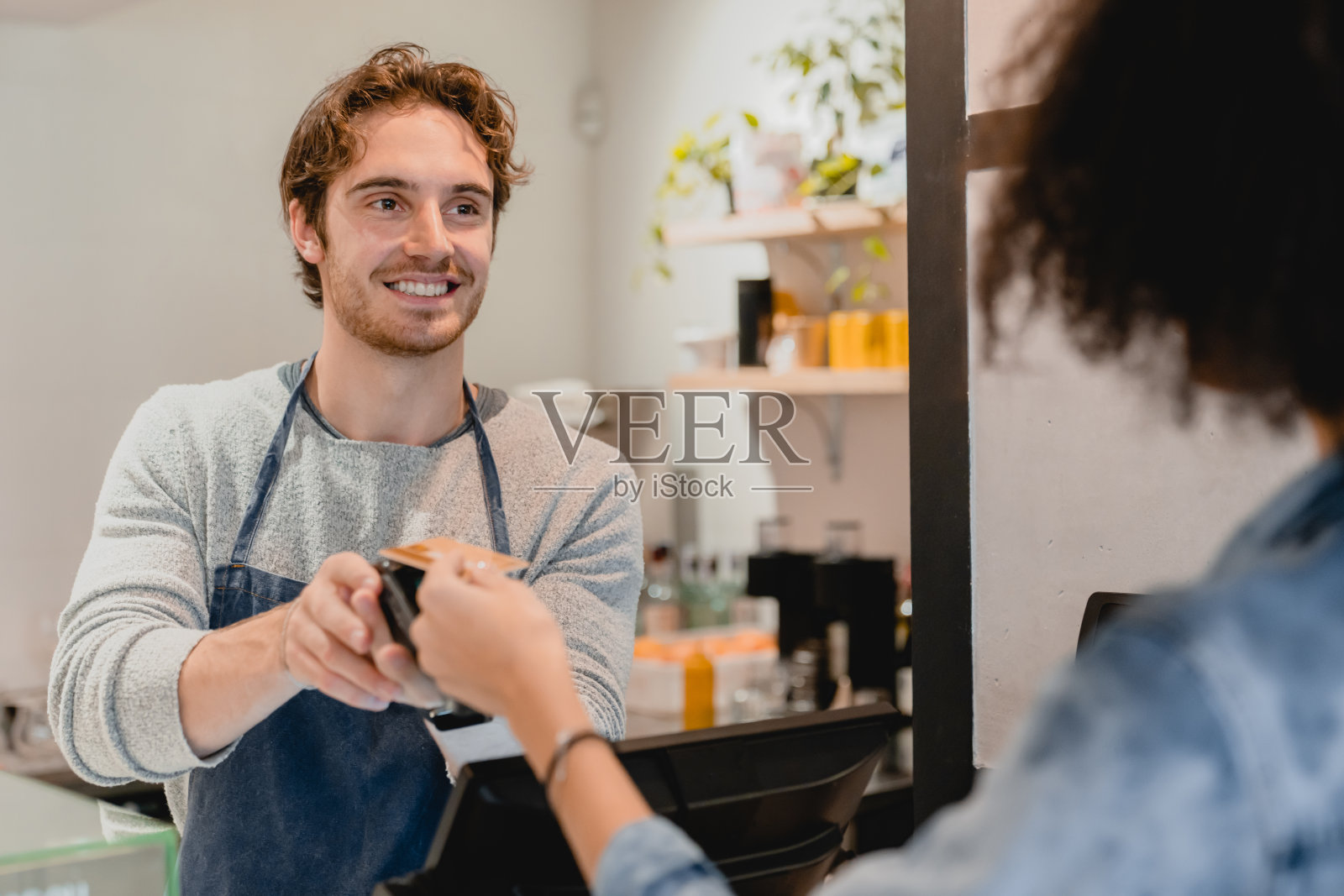 年轻的白人服务员在咖啡馆用刷卡机为顾客服务照片摄影图片