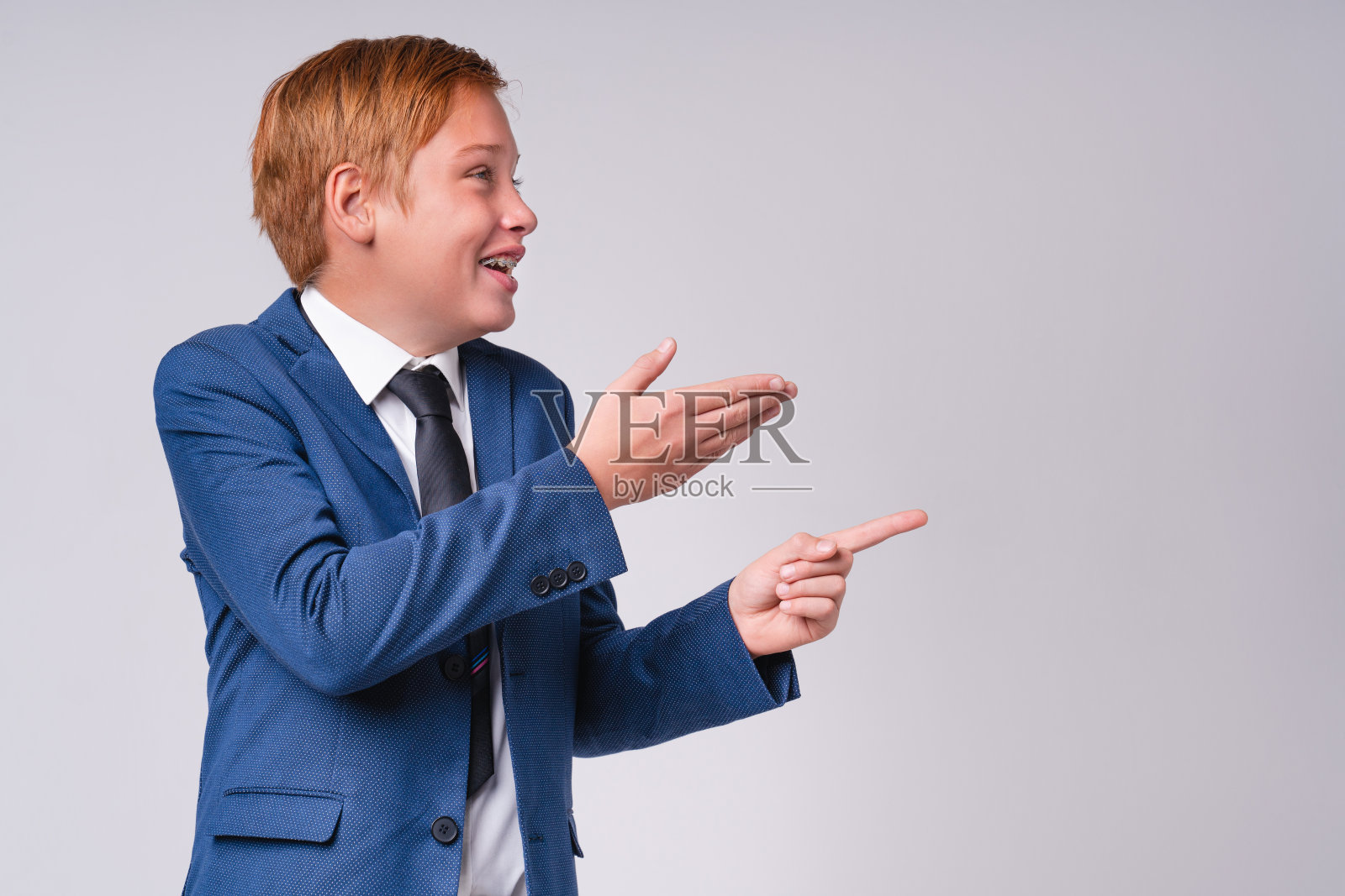 身着正装的红发男孩兴奋地指着灰色背景下孤立的文案空间照片摄影图片