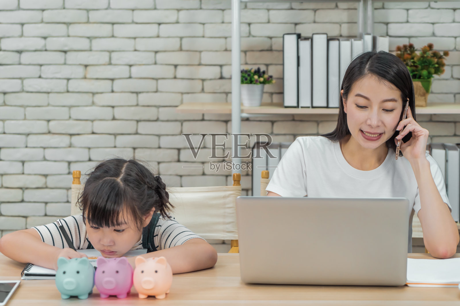 一位亚洲母亲在家里工作的时候教她的女儿关于财务储蓄和商业。照片摄影图片