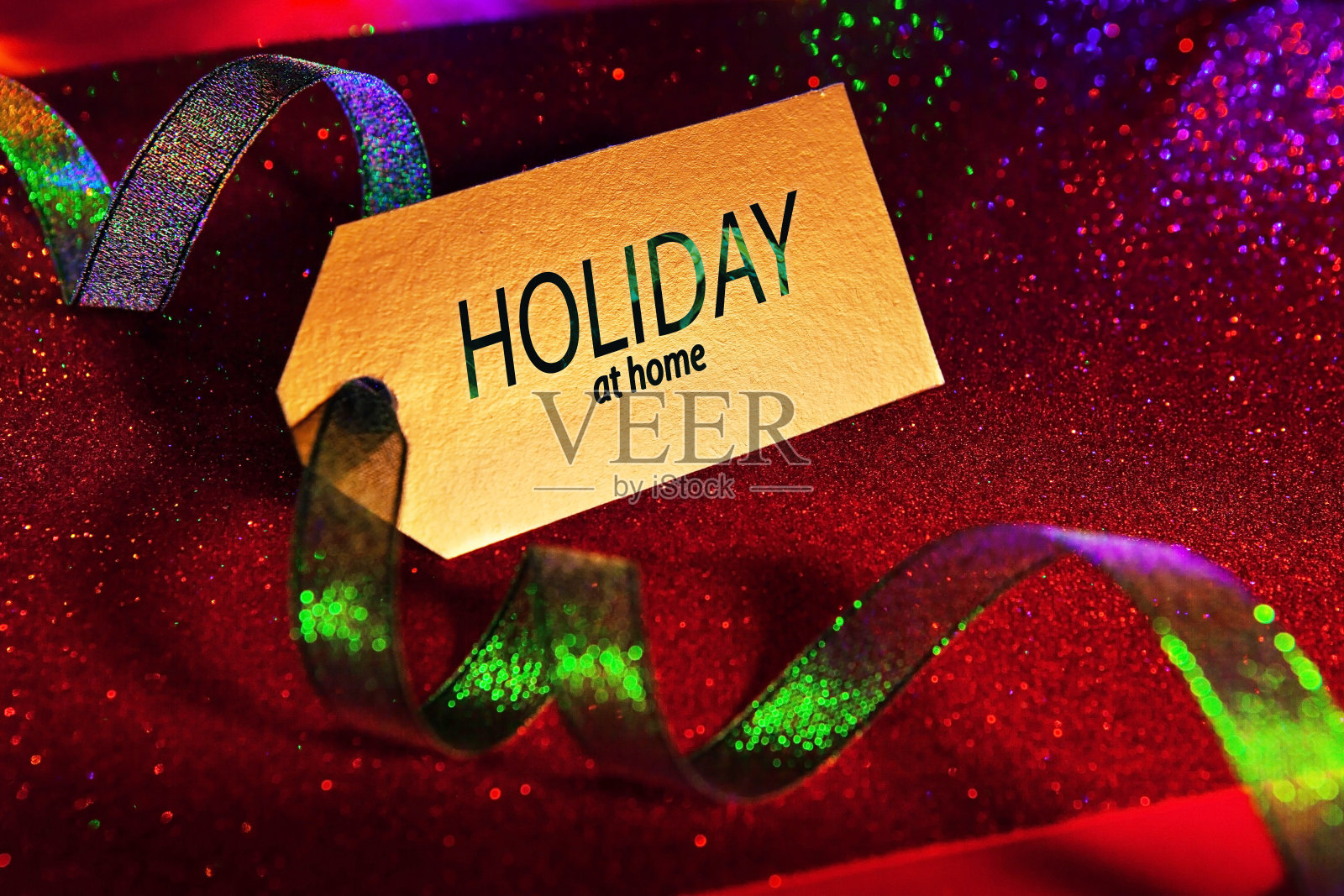 假日在家-标签上的文字，配上鲜艳的绿色丝带，明亮的节日豪华背景，闪闪发光的红色。照片摄影图片