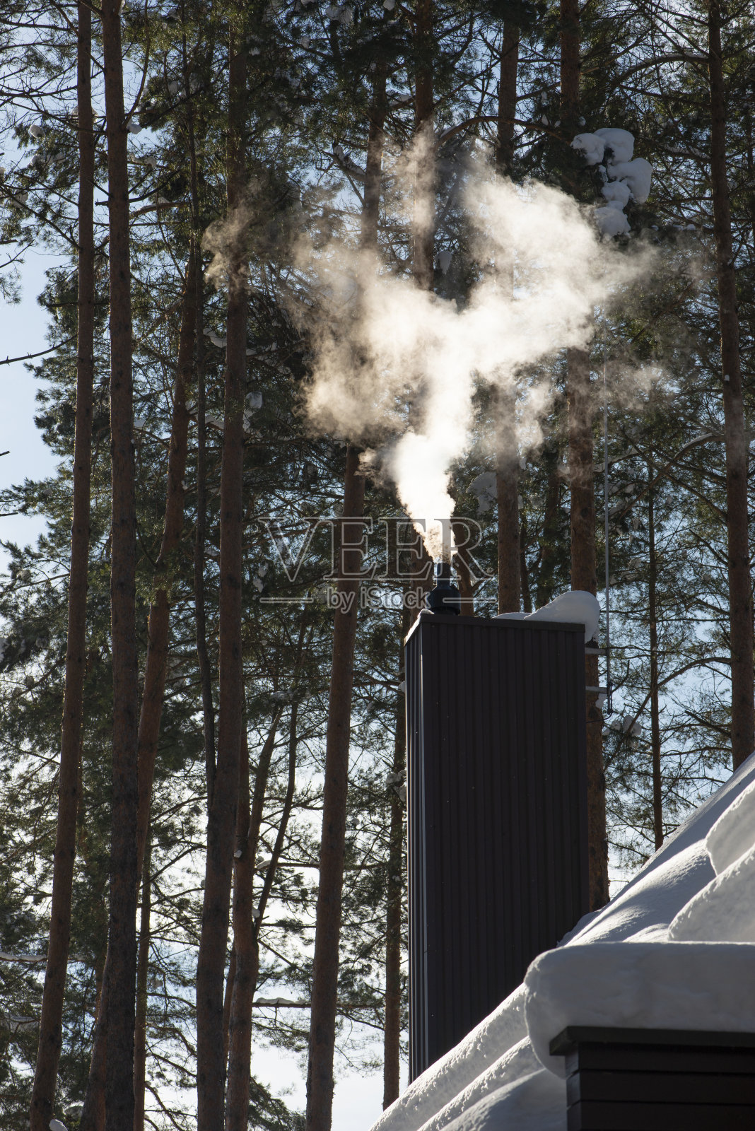 雪屋顶上现代烟囱管冒出的烟雾，背景是森林照片摄影图片