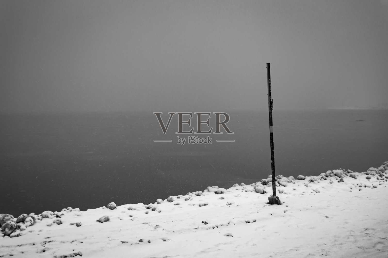 在芝加哥市区，一根单极标记卡在冰冻的冰和沙子上，湖面平静，天空雾蒙蒙照片摄影图片