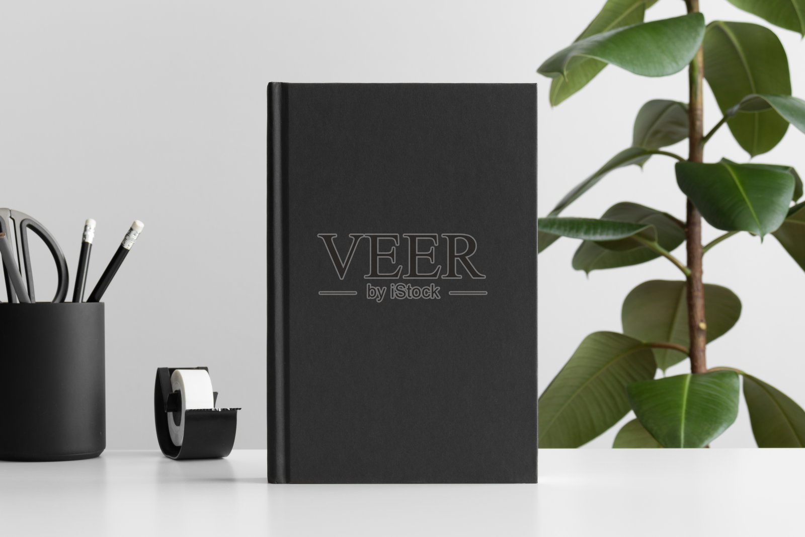 黑色的书模型与工作配件在一个白色的桌子和一棵榕树植物。照片摄影图片