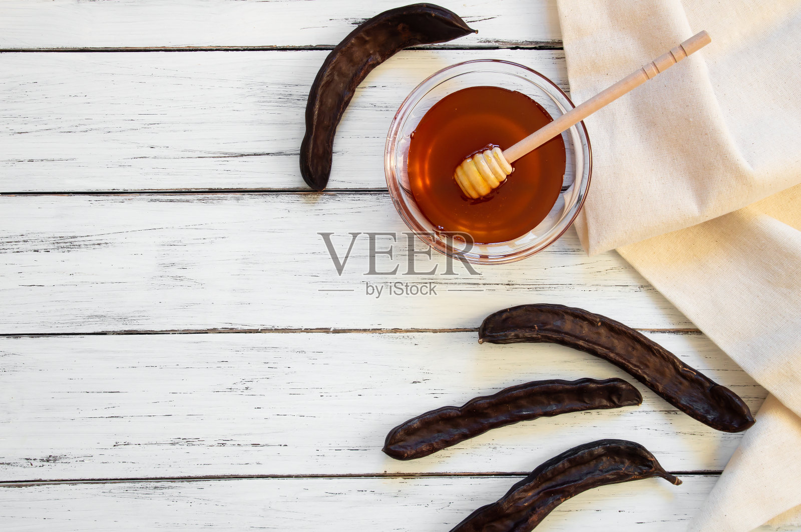 角豆蜂蜜概念，蜂蜜在玻璃碗与角豆荚在白色木桌，健康食品照片摄影图片
