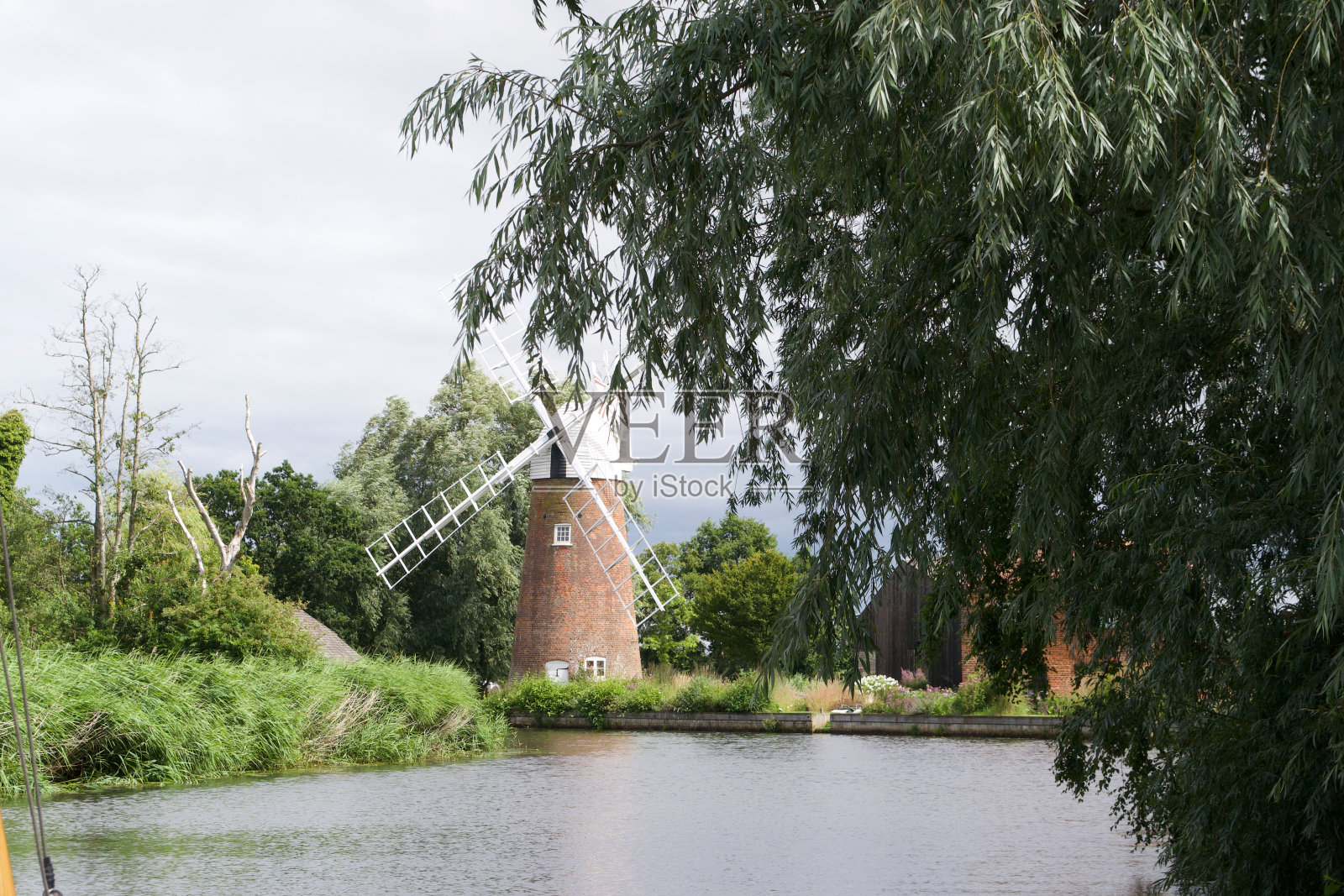 传统的风车(风泵)在河岸与树木照片摄影图片
