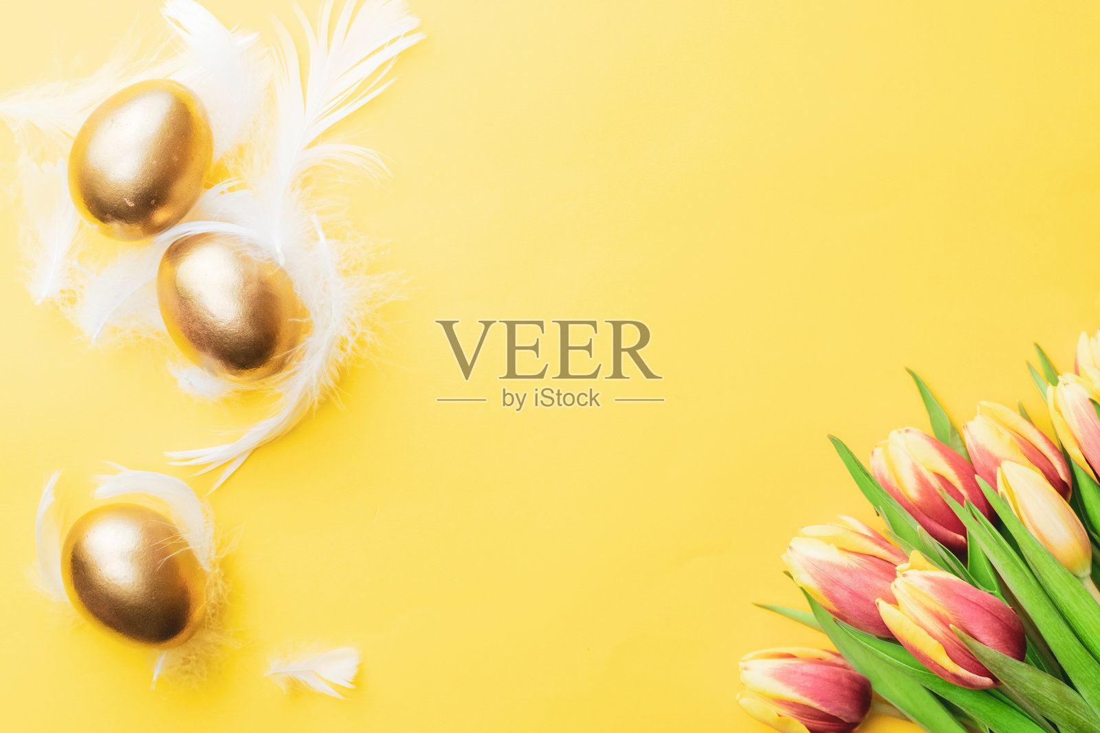 复活节彩蛋黄金。金色彩蛋篮子与春天的郁金香，白色羽毛在柔和的黄色背景在快乐复活节装饰。庆祝复活节的设计。平躺，俯视图。照片摄影图片