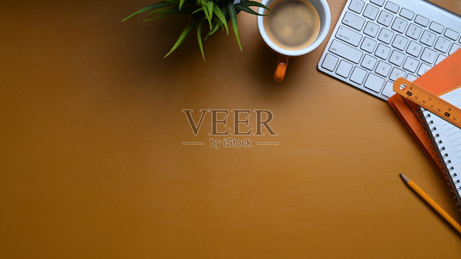 顶视图时尚的工作场所，无线键盘，植物，咖啡杯和复制空间在橙色皮革。照片摄影图片