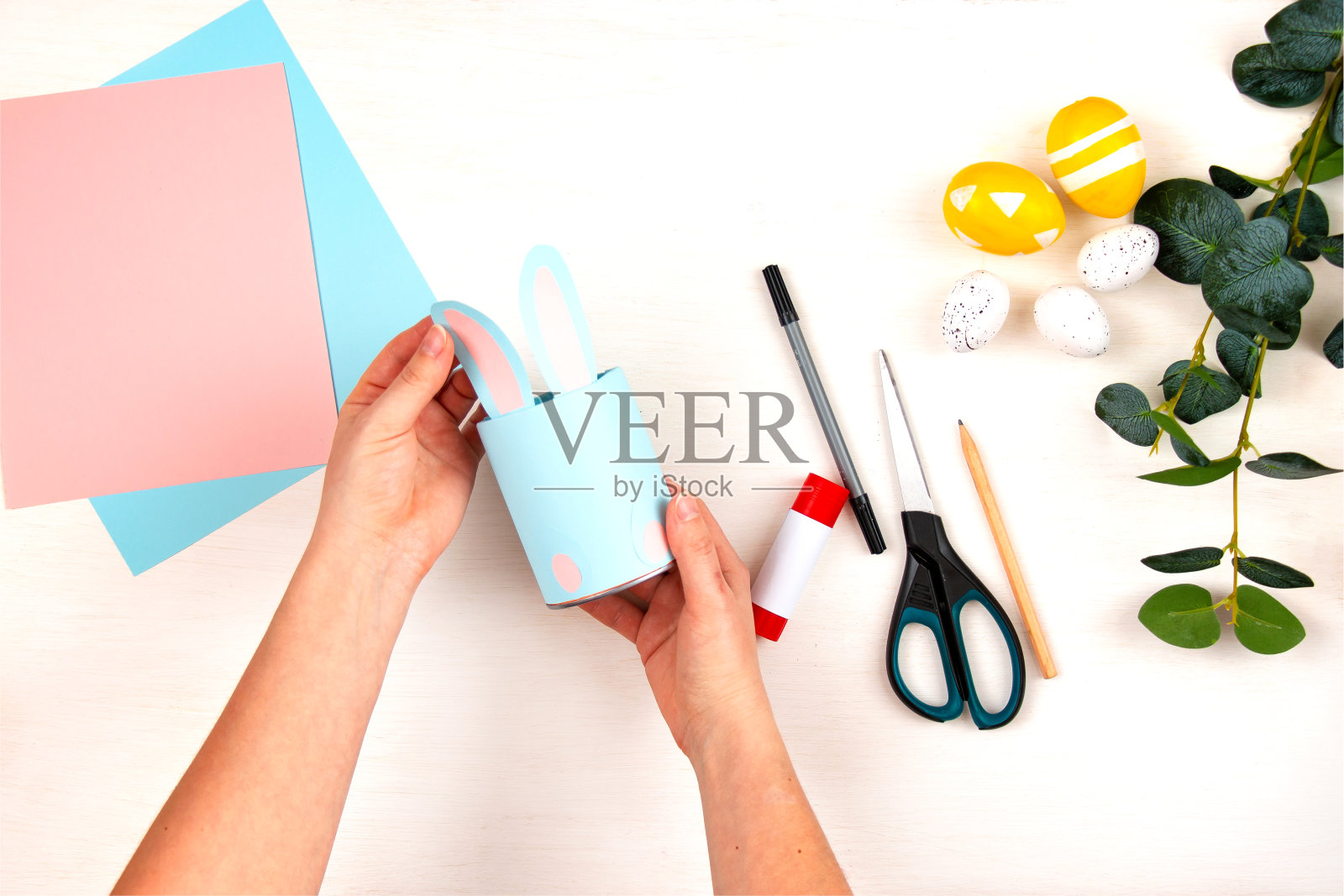 工艺制作流程。在一张轻便的木桌上，女性的手拿着一个装铅笔的玻璃杯。一步一步。从以上观点。孩子们的复活节工艺品。第9步。照片摄影图片