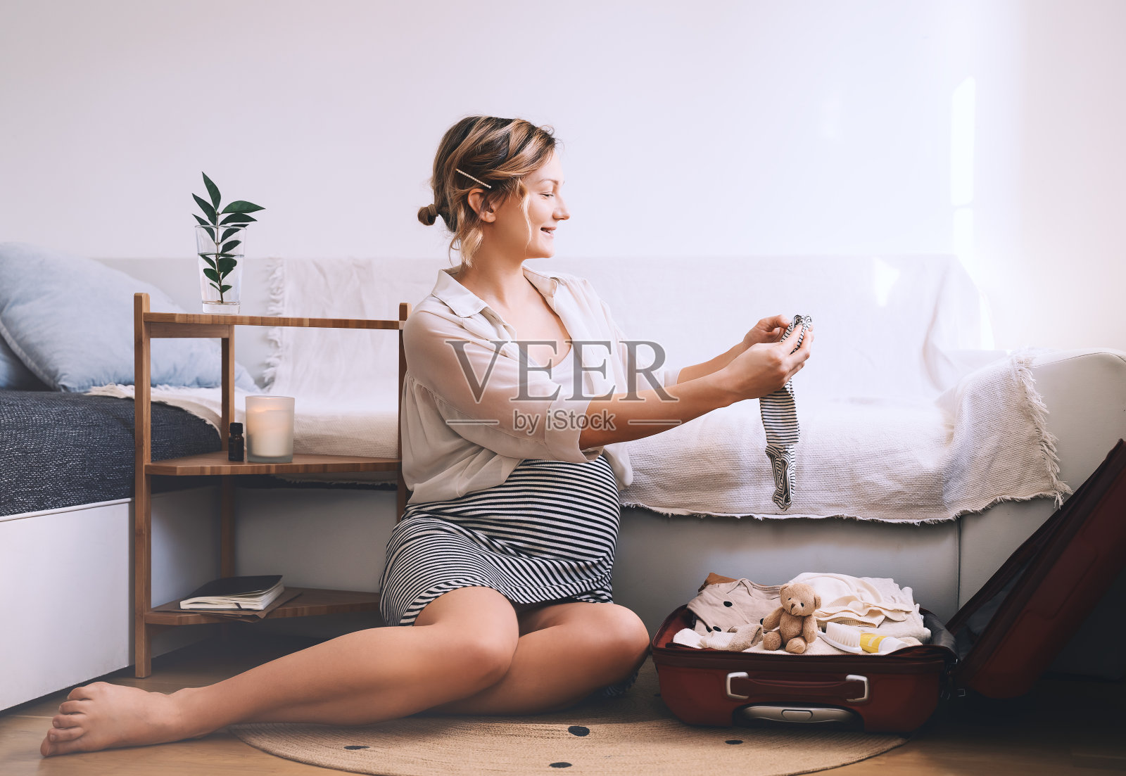 孕妇正收拾行囊前往妇产医院准备分娩。年轻快乐的妈妈带着旅行行李，把婴儿的衣服放在家里。照片摄影图片