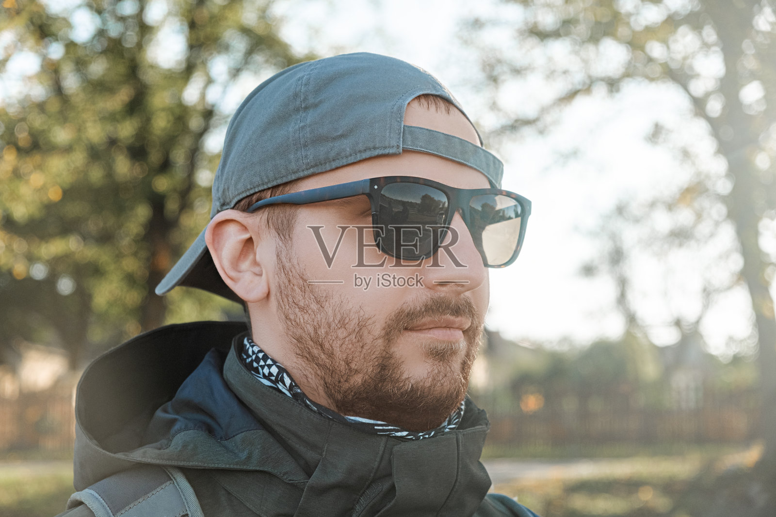 一个戴着太阳镜和棒球帽的大胡子男人，在一个阳光明媚的秋日里，背景是树木和大自然。在乡村度假、隐居或徒步旅行的概念照片摄影图片