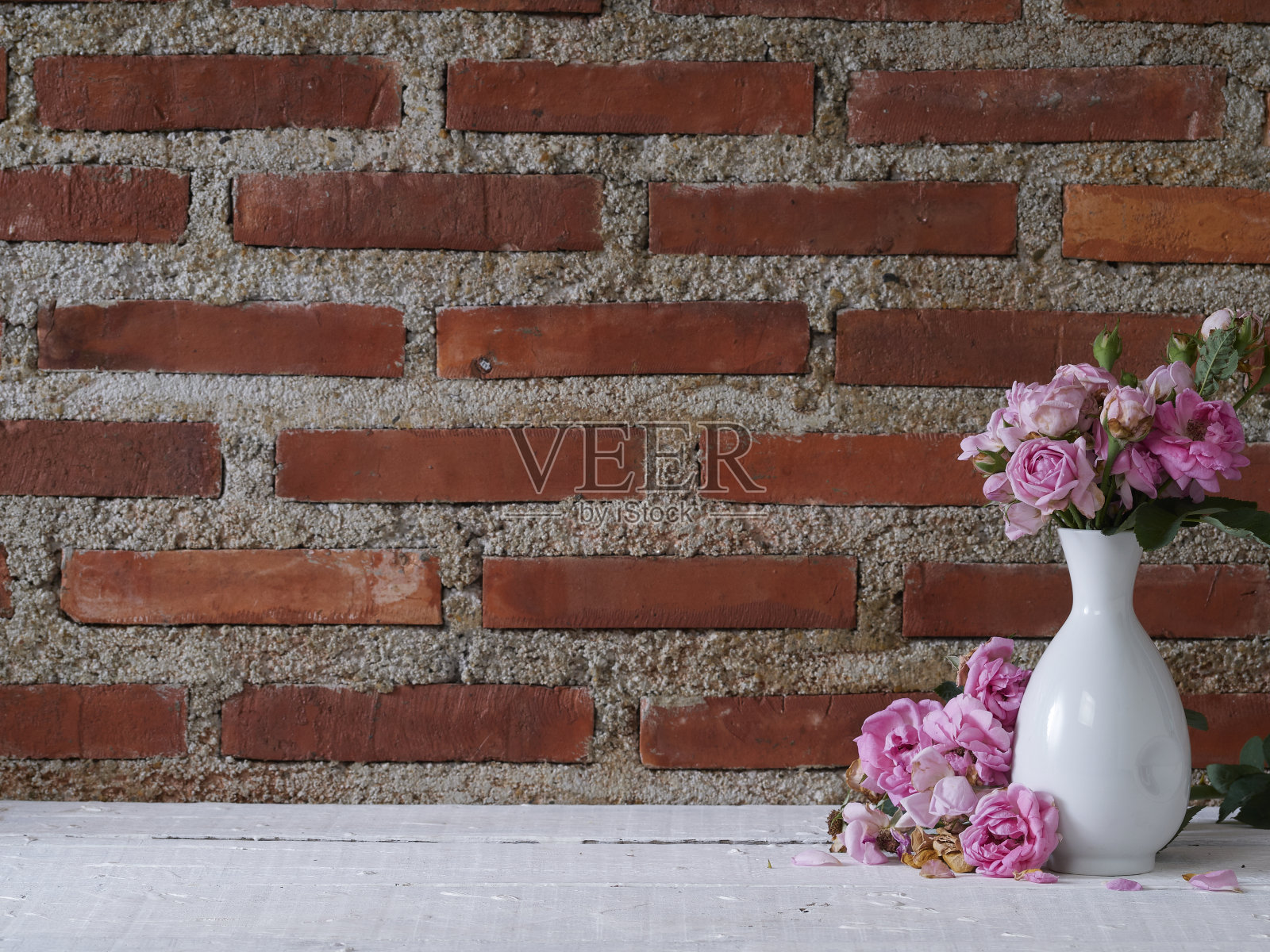 以砖墙为背景的白桌上，插着玫瑰花的花瓶照片摄影图片