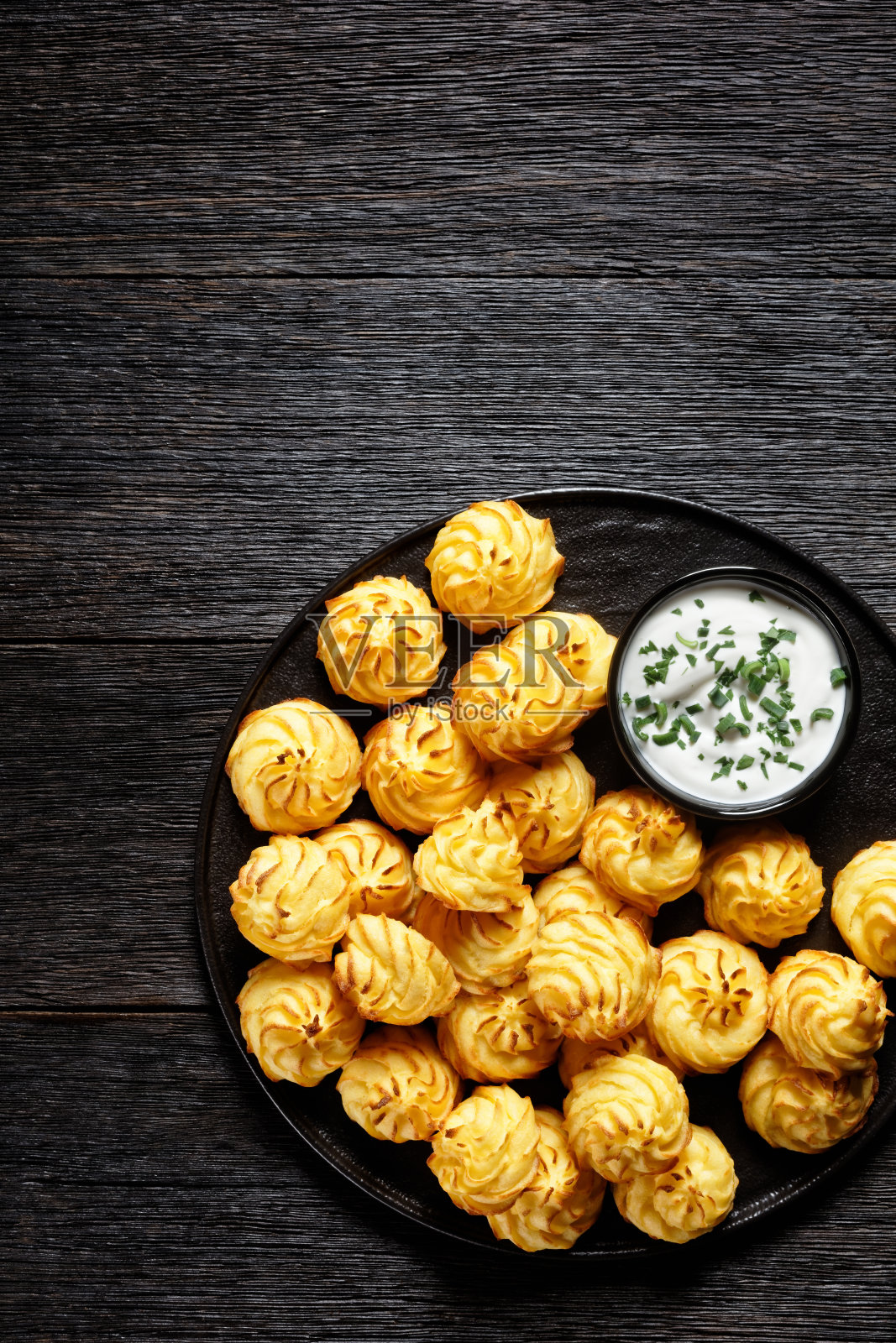 公爵夫人土豆，土豆泥以装饰性的漩涡状排列，在烤箱中呈棕色，配以白色酱汁，放在黑色的盘子上，平铺，空间宽敞照片摄影图片