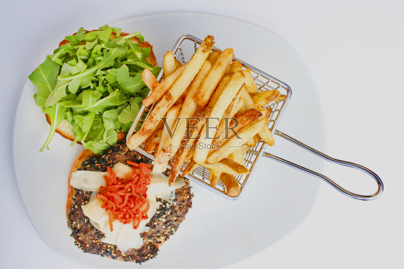 一个汉堡，上面有芝麻肉饼、腌姜、蔬菜和薯条，放在一个金属篮子里照片摄影图片