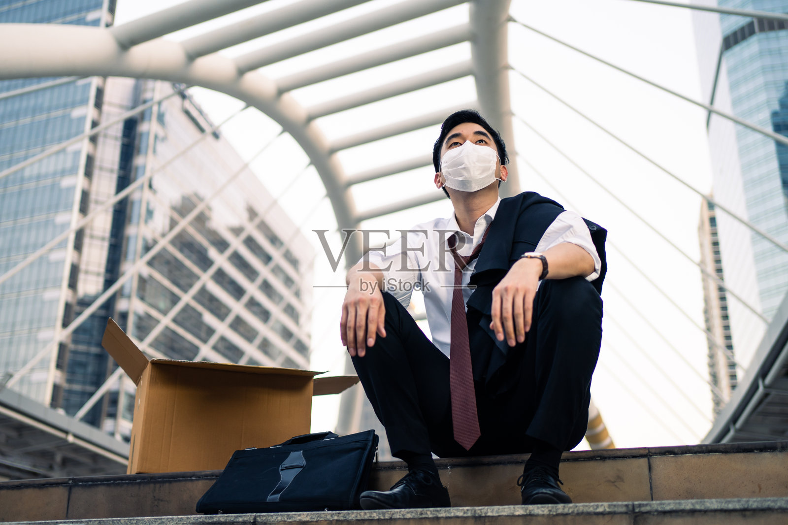 亚洲商人感到悲伤后失业从他的公司。坐在户外的男人感到压力，担心因为世界经济问题而失去工作，因为冠状病毒危机的概念。照片摄影图片